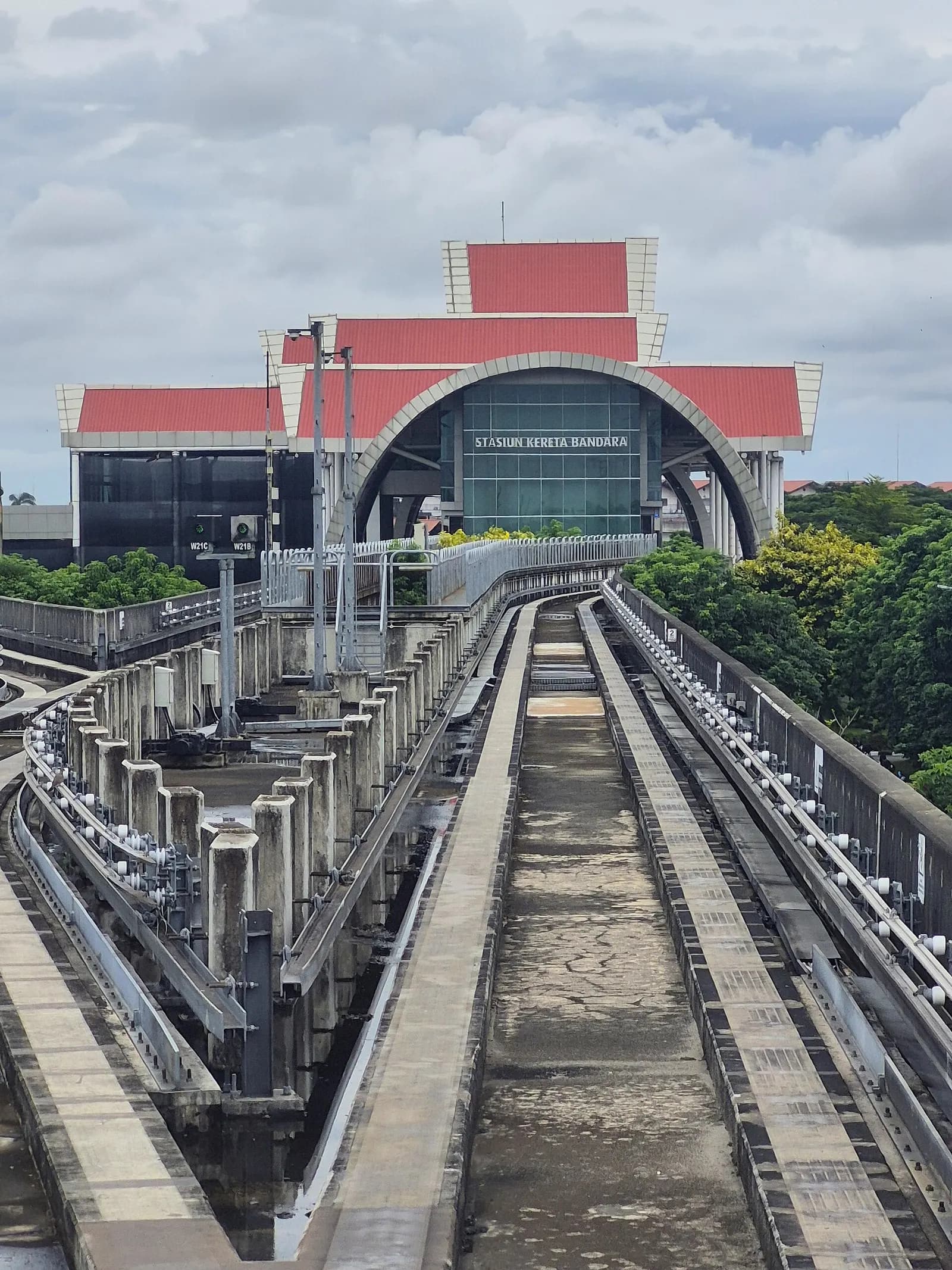 Exterior of the Soekarno-Hatta airport rail station in 2025, with a modern building facade, covered walkways, and connecting roads nearby.