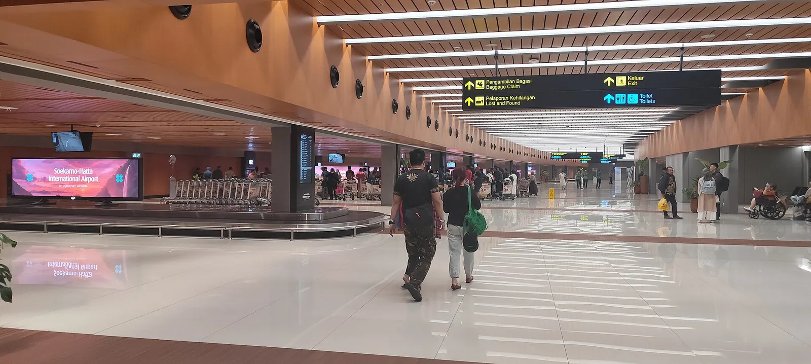 Wide interior view of the Terminal 1C arrivals hall with tiled floors, support columns, directional signage, and passenger walkways.