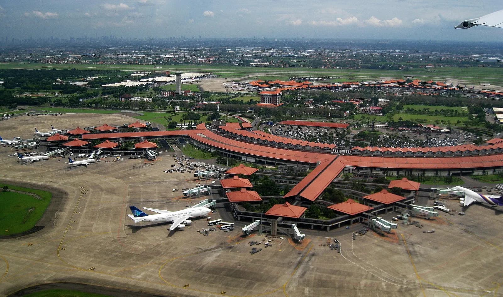 Aerial view of Soekarno-Hatta International Airport showing multiple terminals with distinctive Javanese joglo-style peaked roofs amid runways and taxiways.