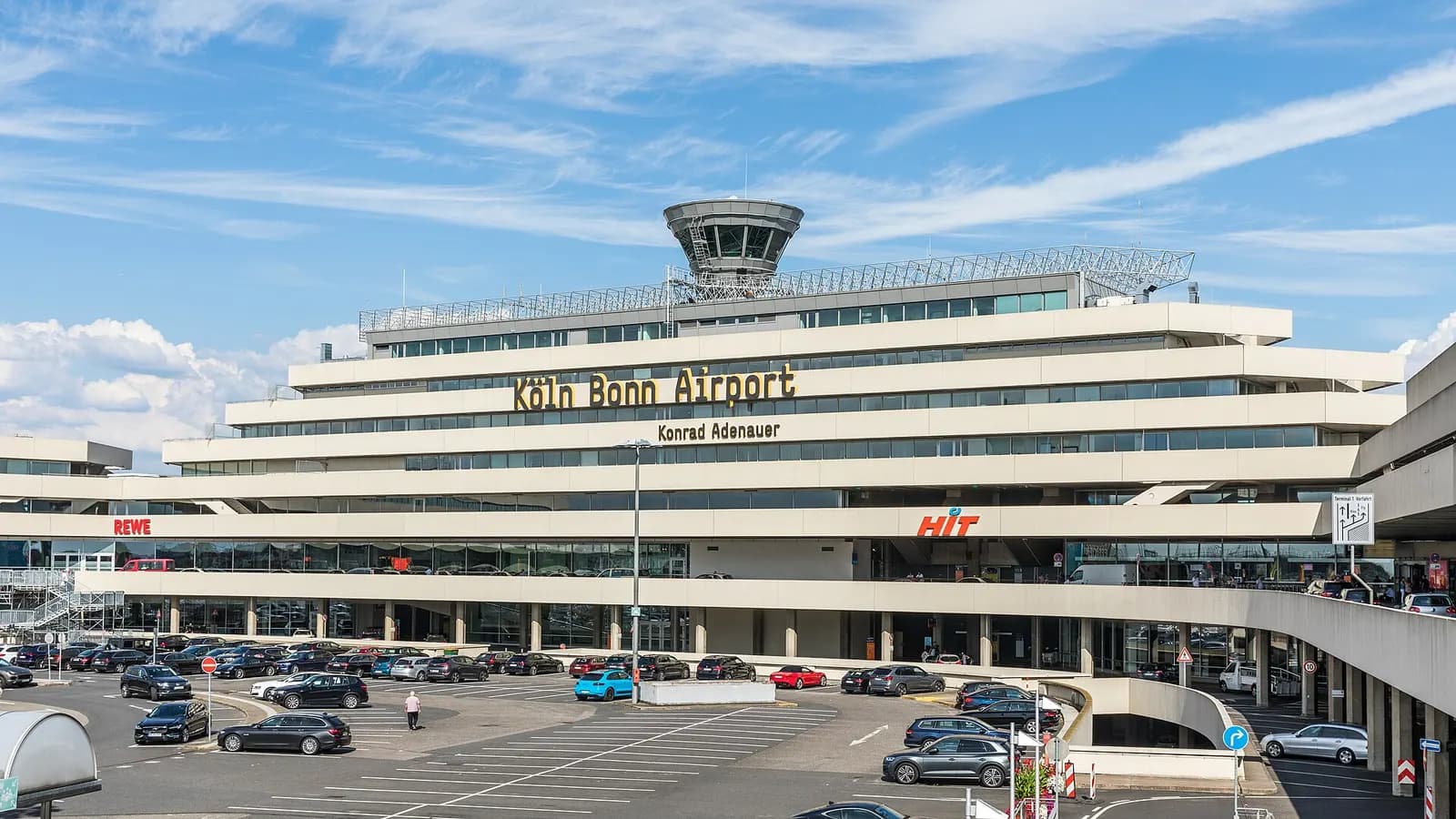 Wide view of the glass-fronted Terminal 1 main building at Cologne Bonn Airport under a partly cloudy sky.