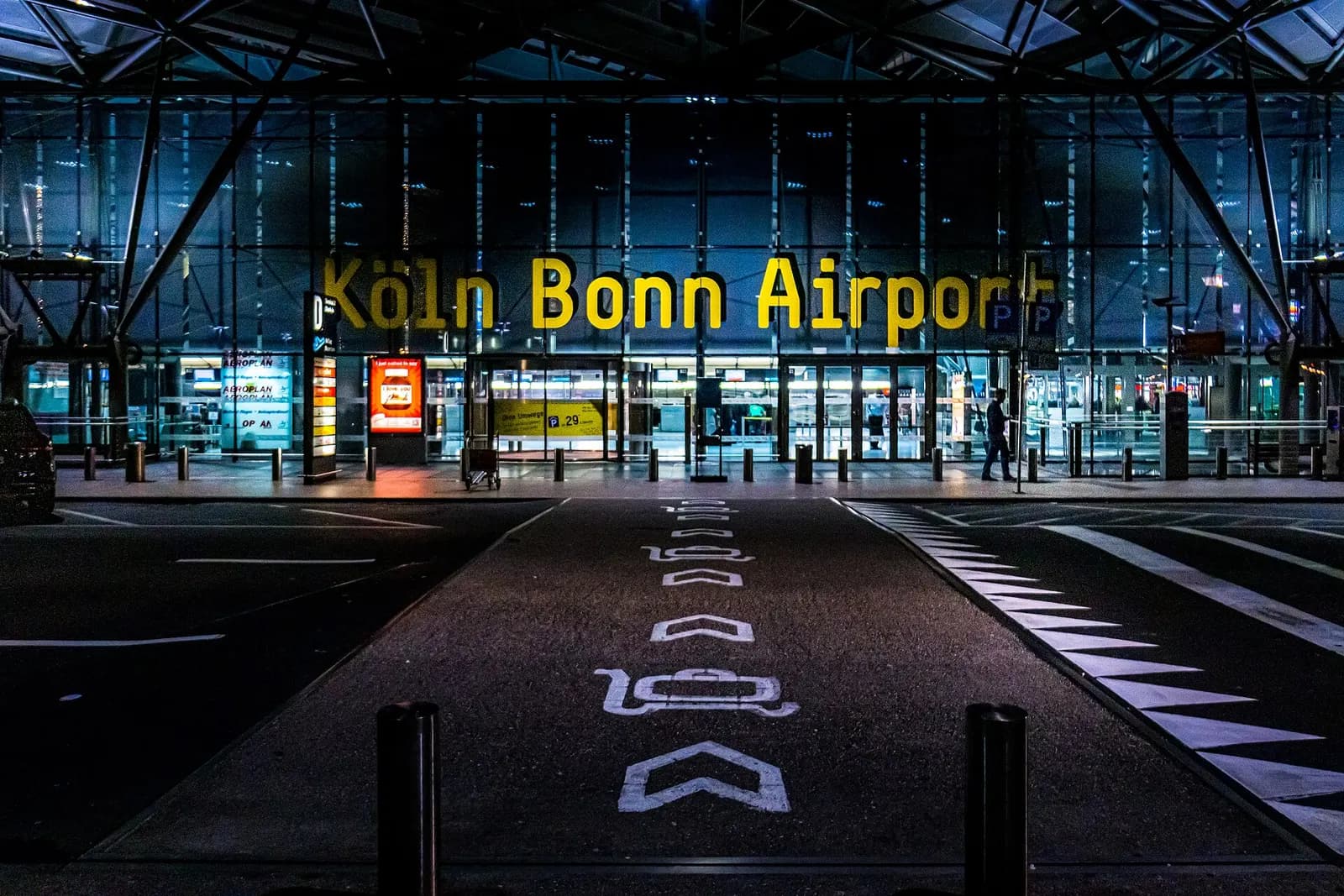 The illuminated entrance area of Konrad Adenauer Airport at Cologne/Bonn at night, with the terminal facade and drop-off zone in view.