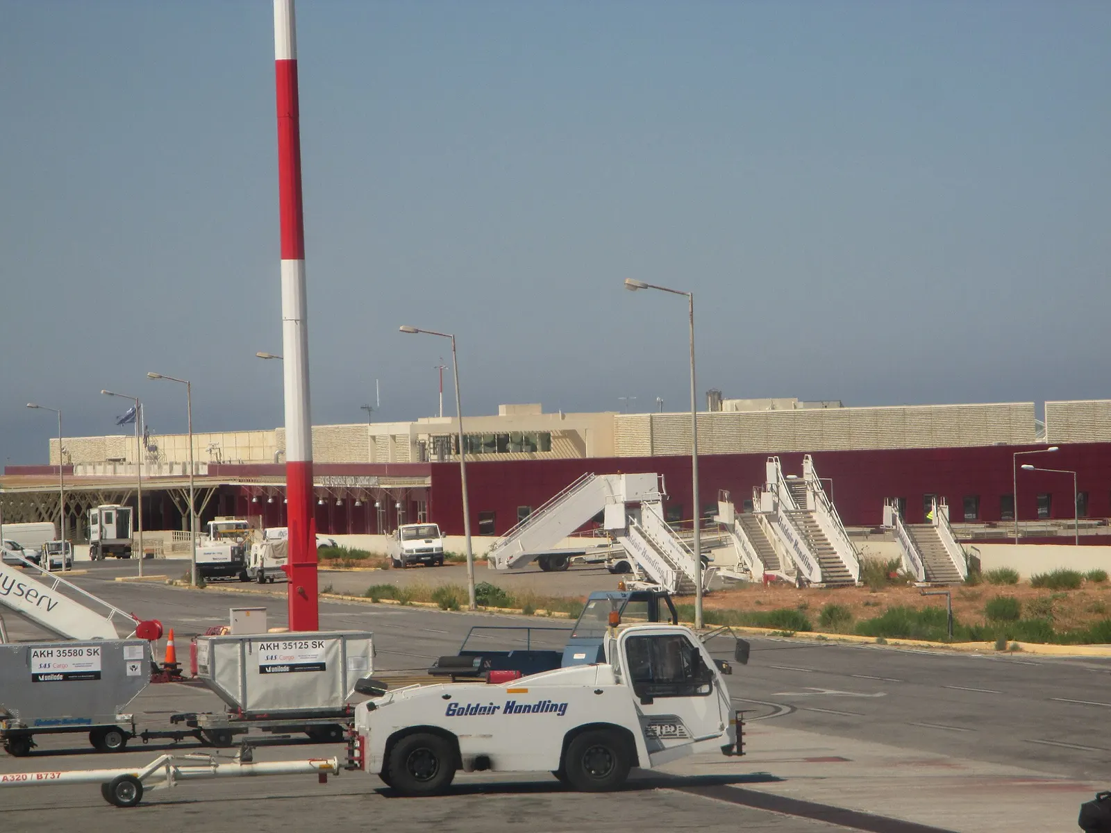 Airside view of the CHQ / LGSA terminal building from an aircraft with ground-handling vehicles.