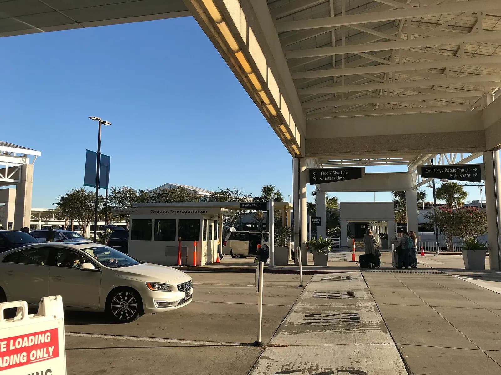 Covered ground-transportation curb at Charleston International with a Ground Transportation booth and signs for taxi, shuttle, limo, courtesy, public transit and rideshare.