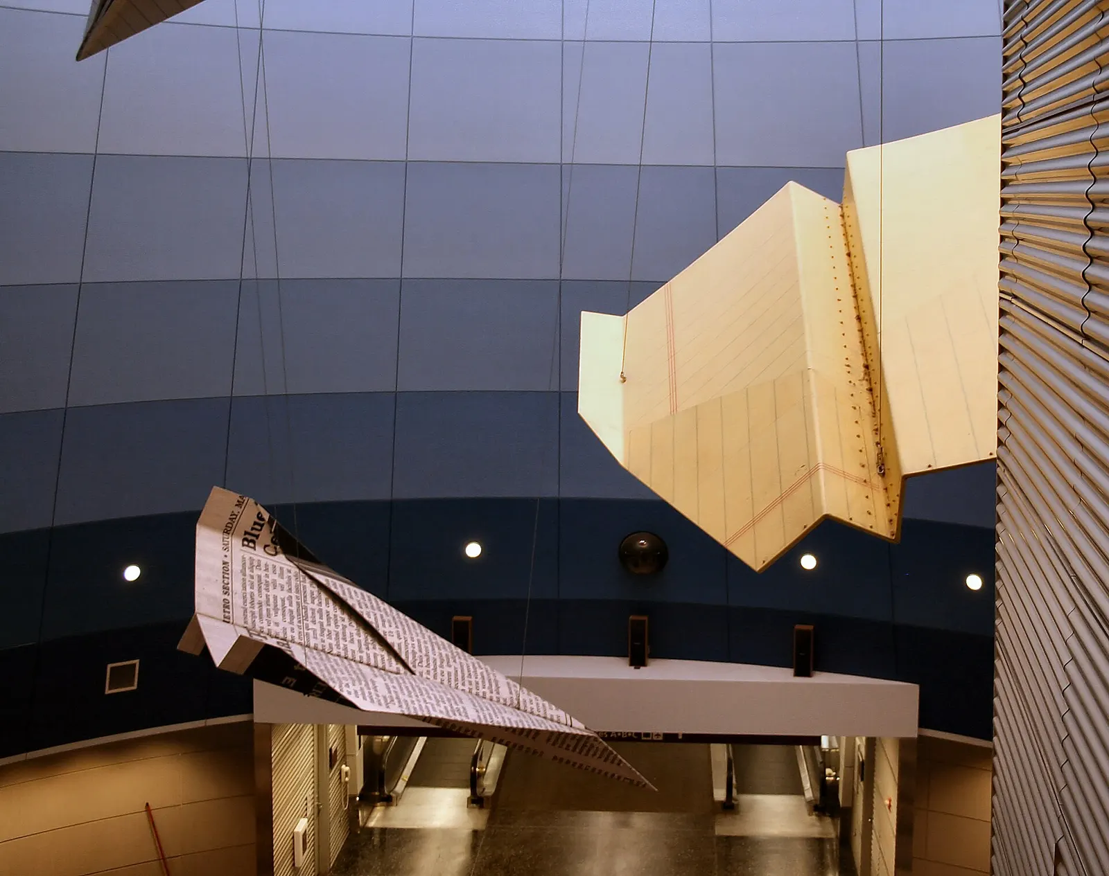 Some of the several giant "paper" airplane sculptures in the Continental terminal of Hopkins International Airport in Cleveland . The airplanes appear to be folded out of yellow legal paper, newspaper, computer paper, notebook paper, and similar materials but are actually made of aluminum covered wi