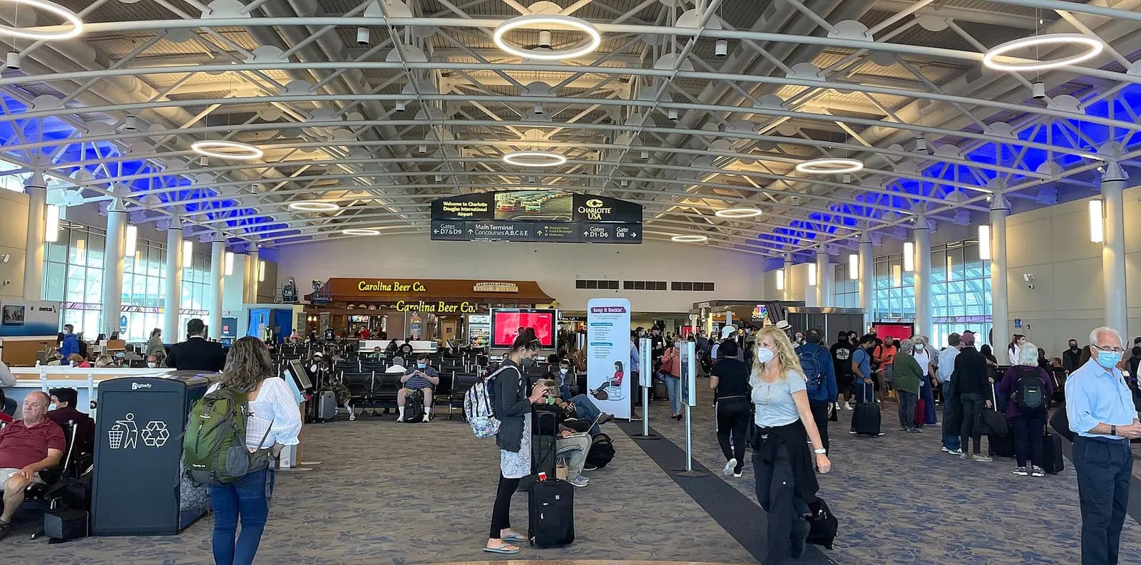 A wide panoramic view along a concourse walkway inside Charlotte Douglas International Airport with gate areas and travelers.