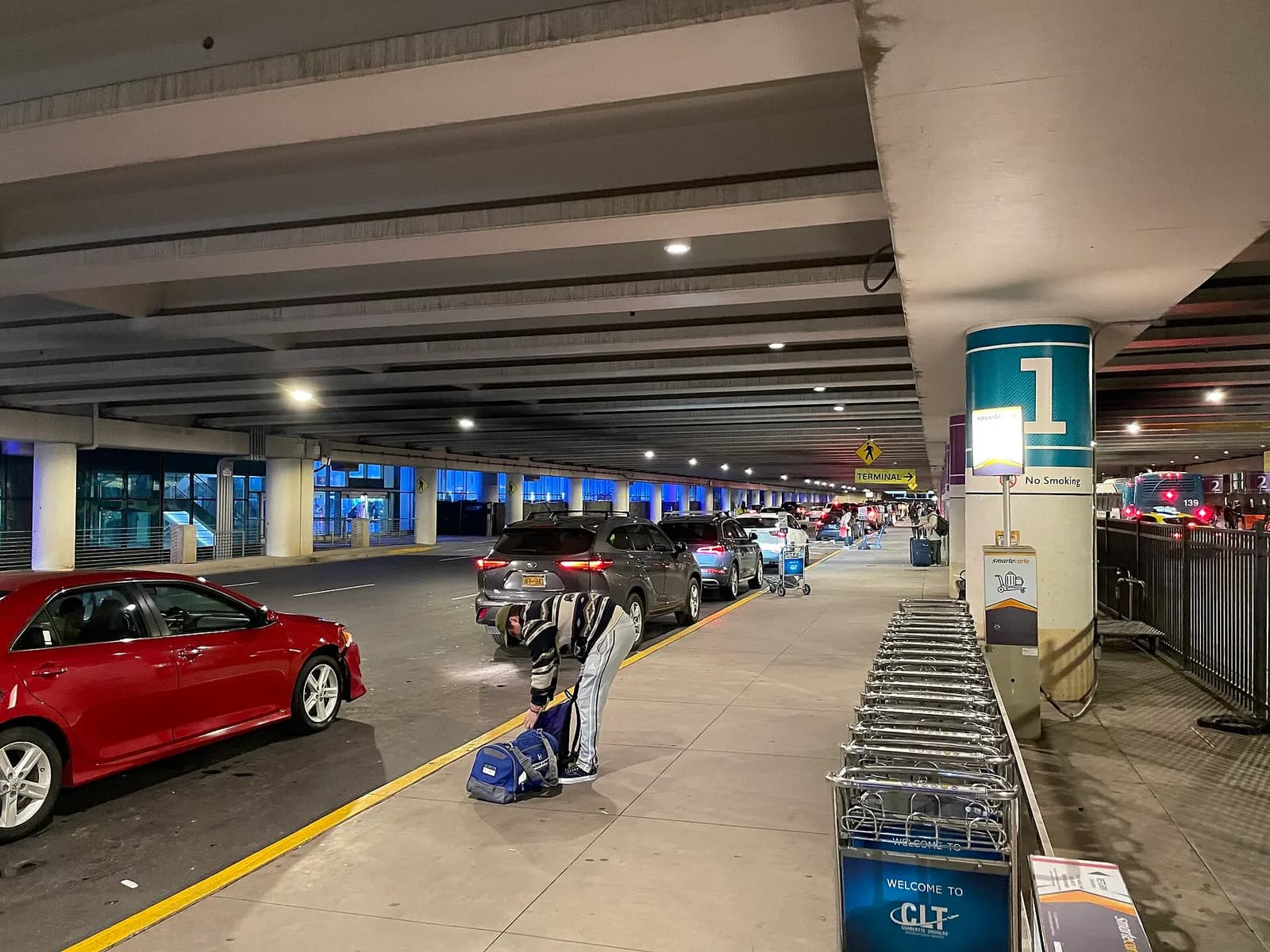 The curbside pickup zone outside Charlotte Douglas International Airport with lane markings, vehicles, and terminal access signage.