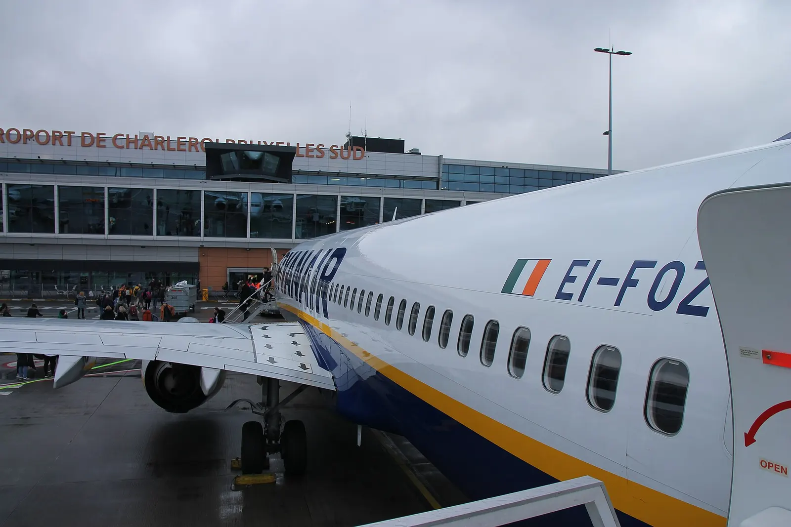 Looking aft along a Ryanair 737 at Charleroi with the Terminal 1 glass wall and rooftop letters in the background.