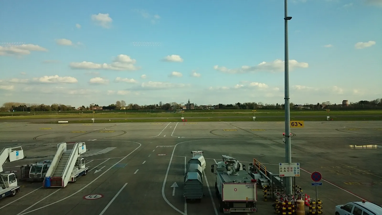 View from Charleroi departure-gate level across the apron toward grass and nearby housing under a clear sky.