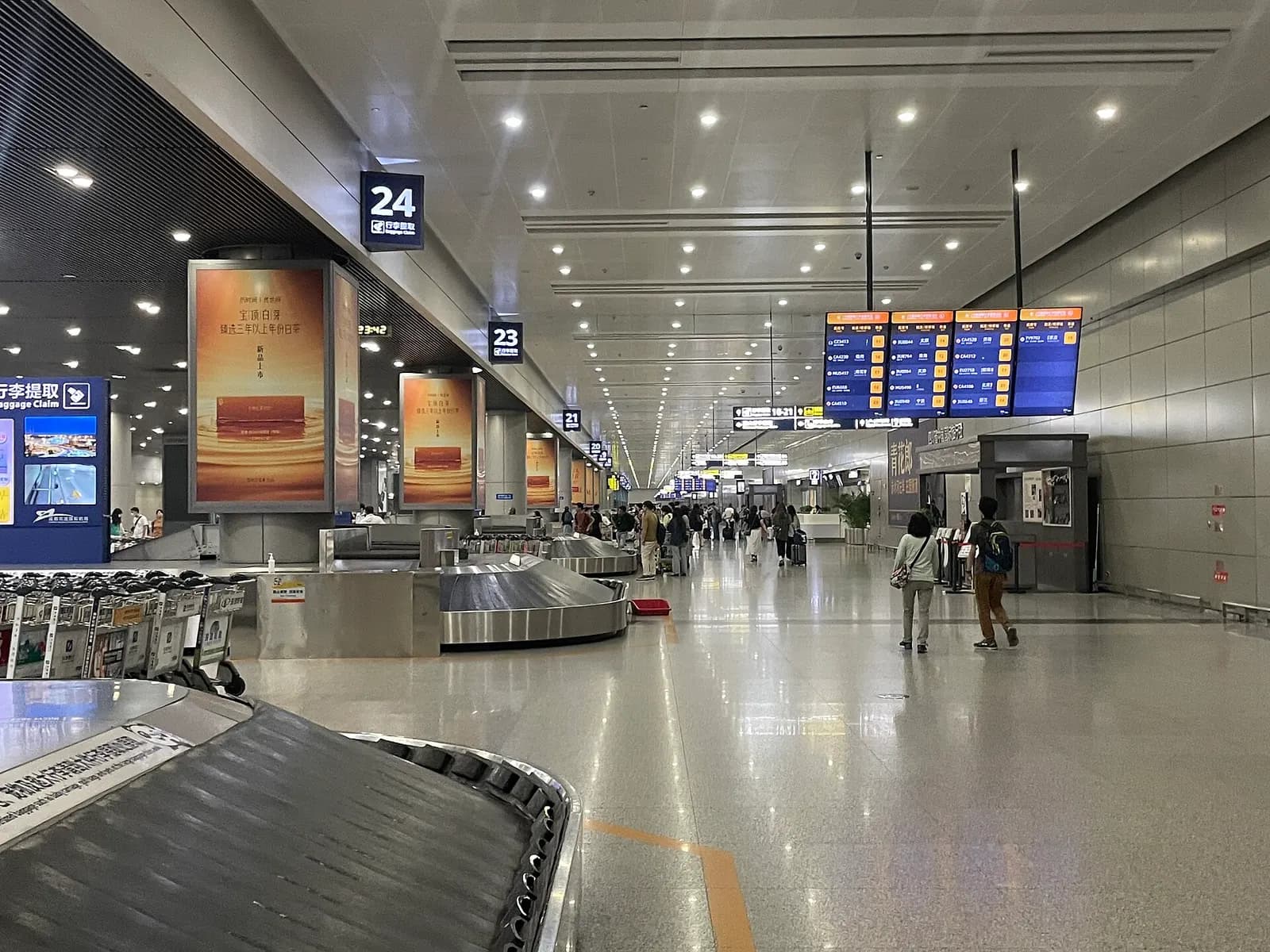 Terminal 2 baggage claim hall with carousels, flight information screens, and arriving passengers collecting luggage.