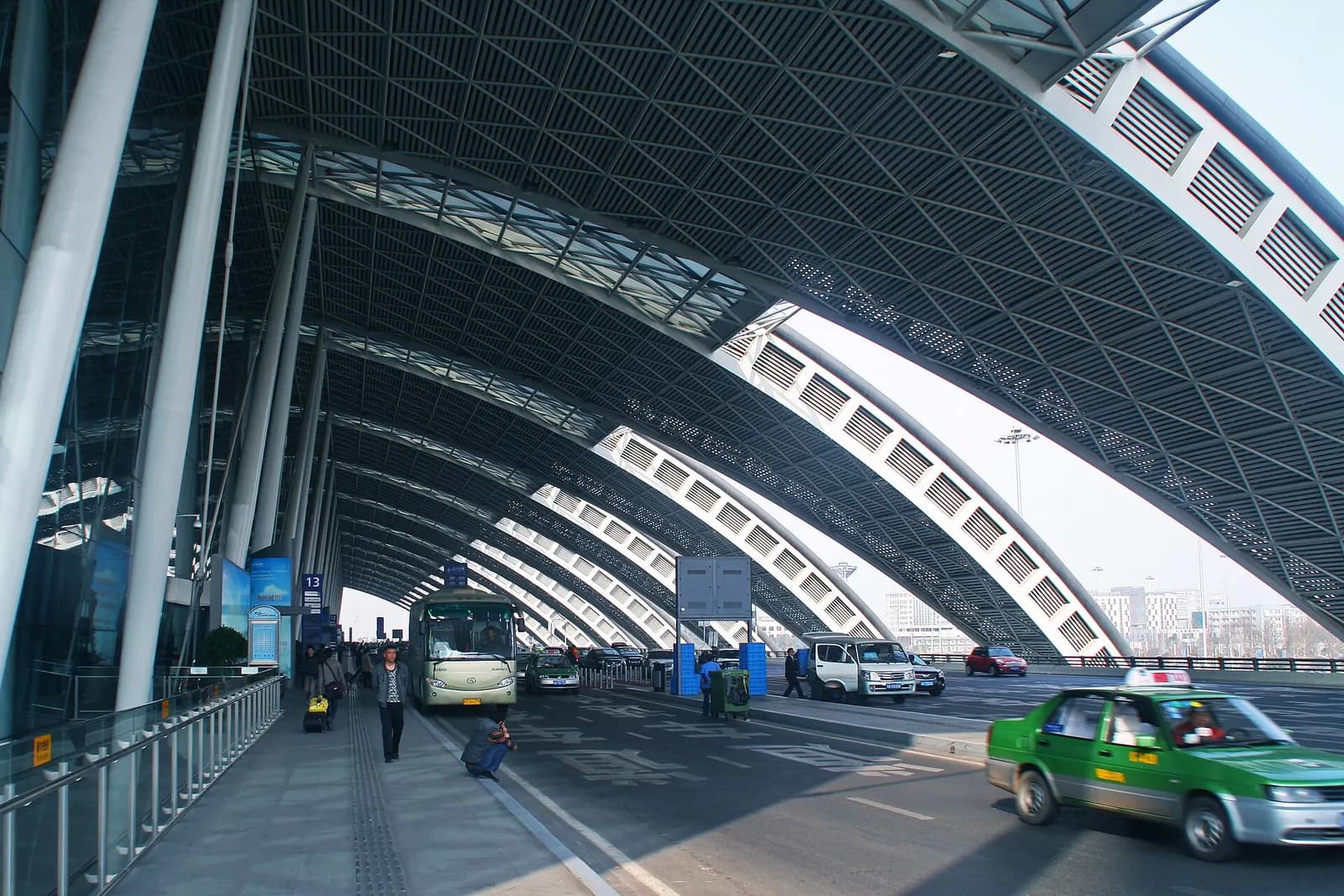 Street-level view outside Terminal 2 showing the terminal facade, entrance canopy, and vehicles in the drop-off area.