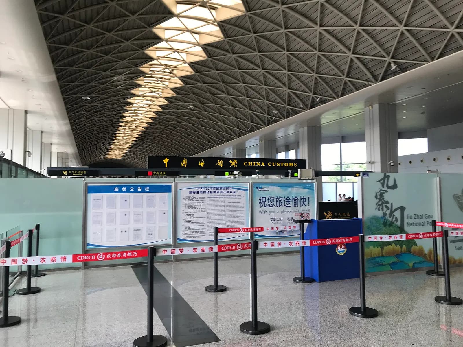 International departure concourse in Terminal 1 with gate seating, retail counters, and large windows separating it from the main terminal.