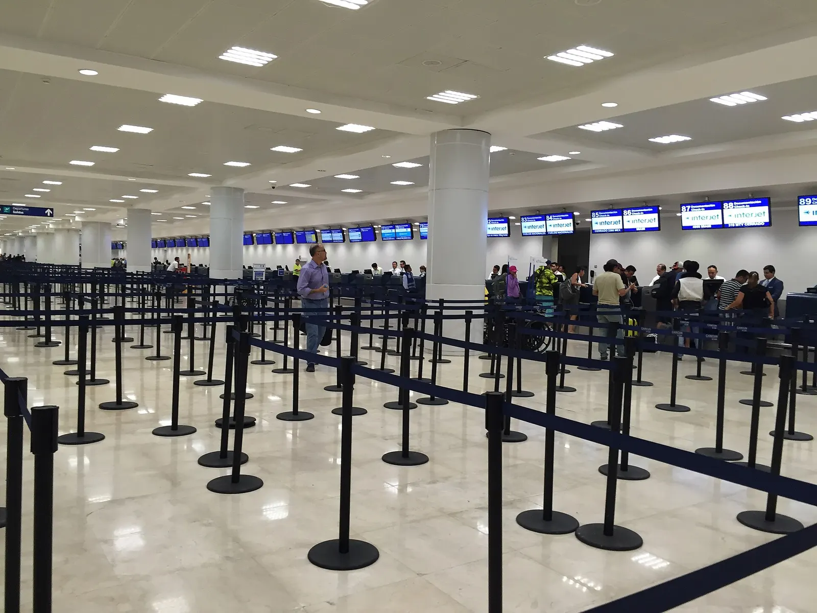 Row of airline check-in counters in Terminal 2 at Cancún International Airport with signage above each desk.