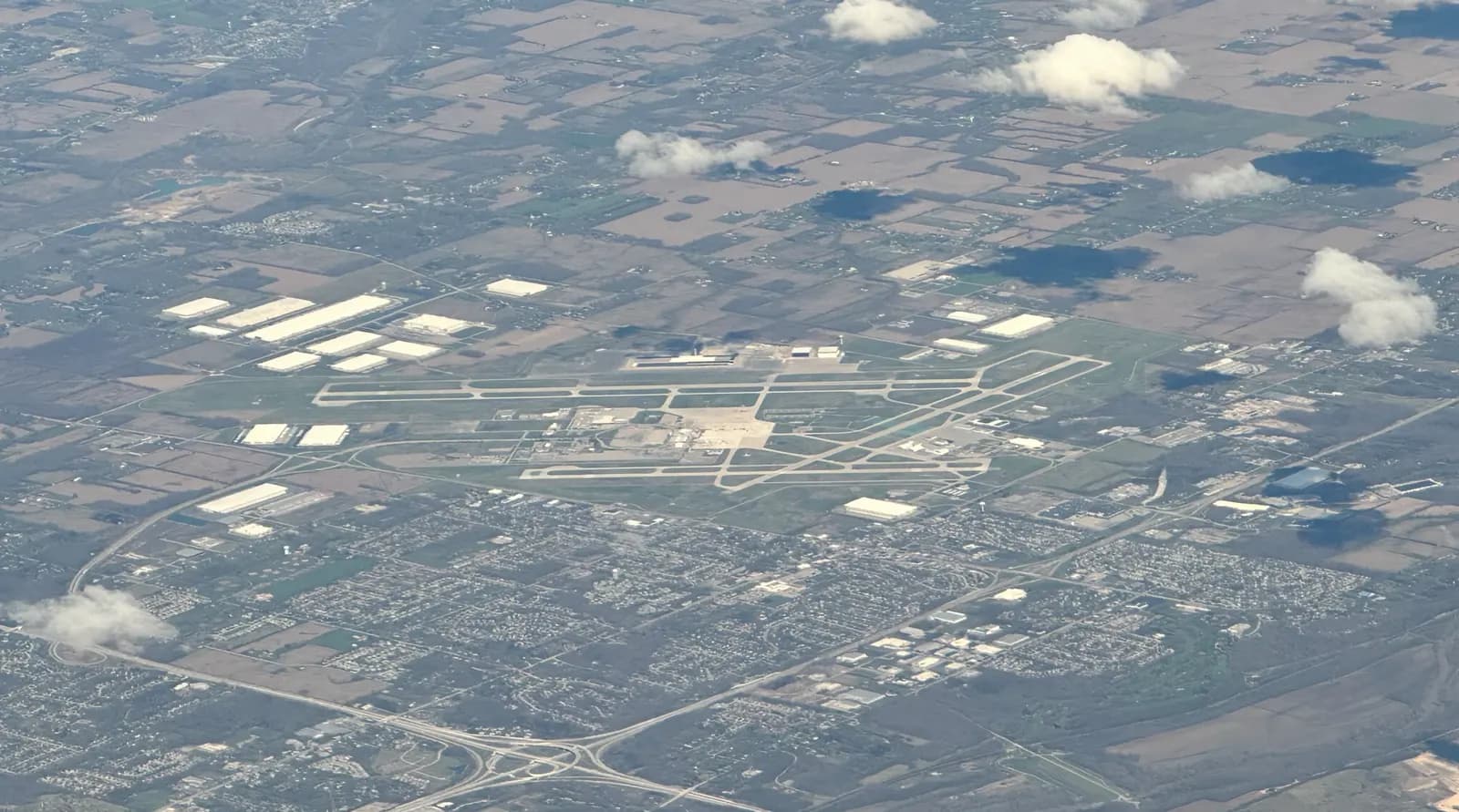 2024 aerial of James M. Cox Dayton International Airport taken from a commercial flight, showing the civil terminal, garage, and parallel runways.