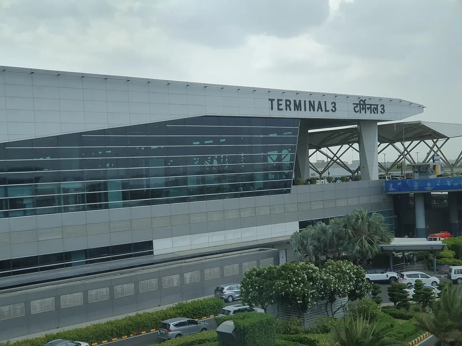 Spacious main concourse of Terminal 3 at Indira Gandhi International Airport with high ceilings, glass walls, and travelers moving through the departures area.