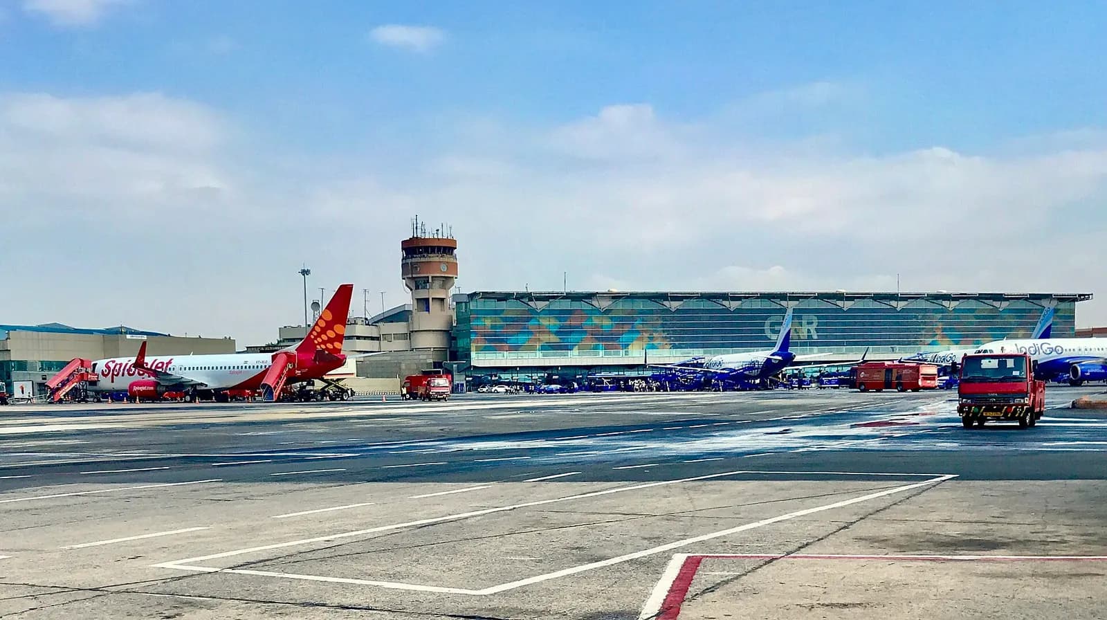Terminal 1 building seen from the airside aircraft parking area at Indira Gandhi International Airport with parked planes in the foreground.