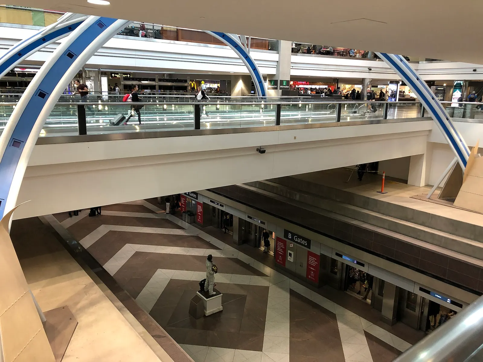 Escalators and walkways converge at a central transit hub in the middle of Concourse B at Denver International Airport.