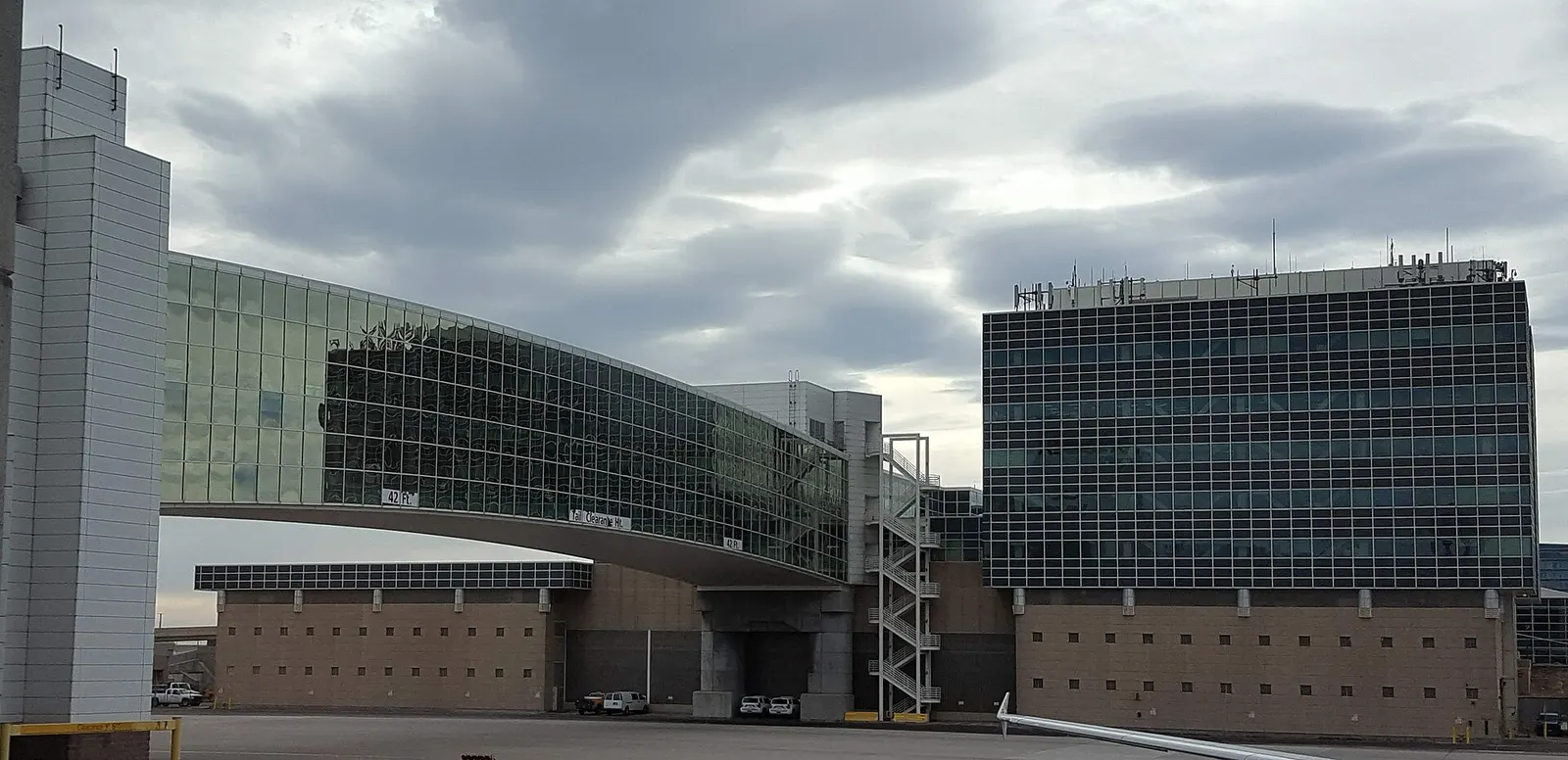 A covered passenger bridge extends from the Jeppesen Terminal toward Concourse A past the Airport Office Building at Denver International Airport.