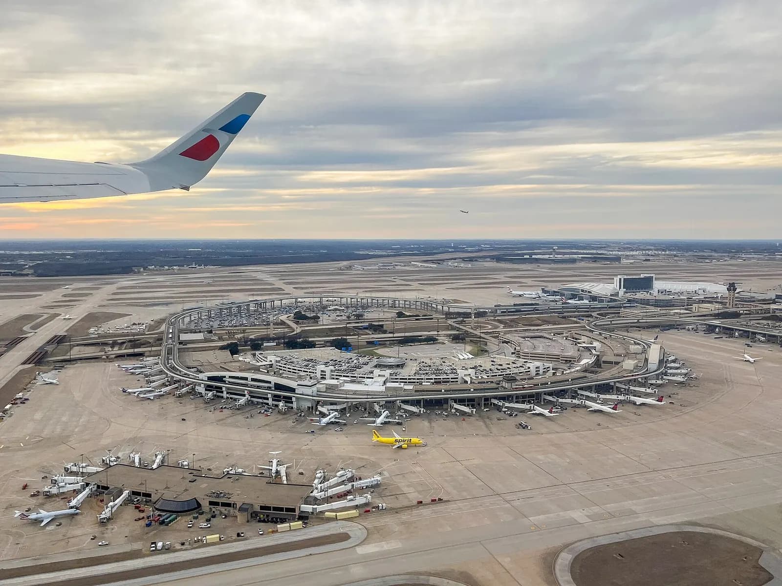 View from an airplane window during takeoff showing DFW Terminal E, adjacent gates, and a satellite terminal on the tarmac below.