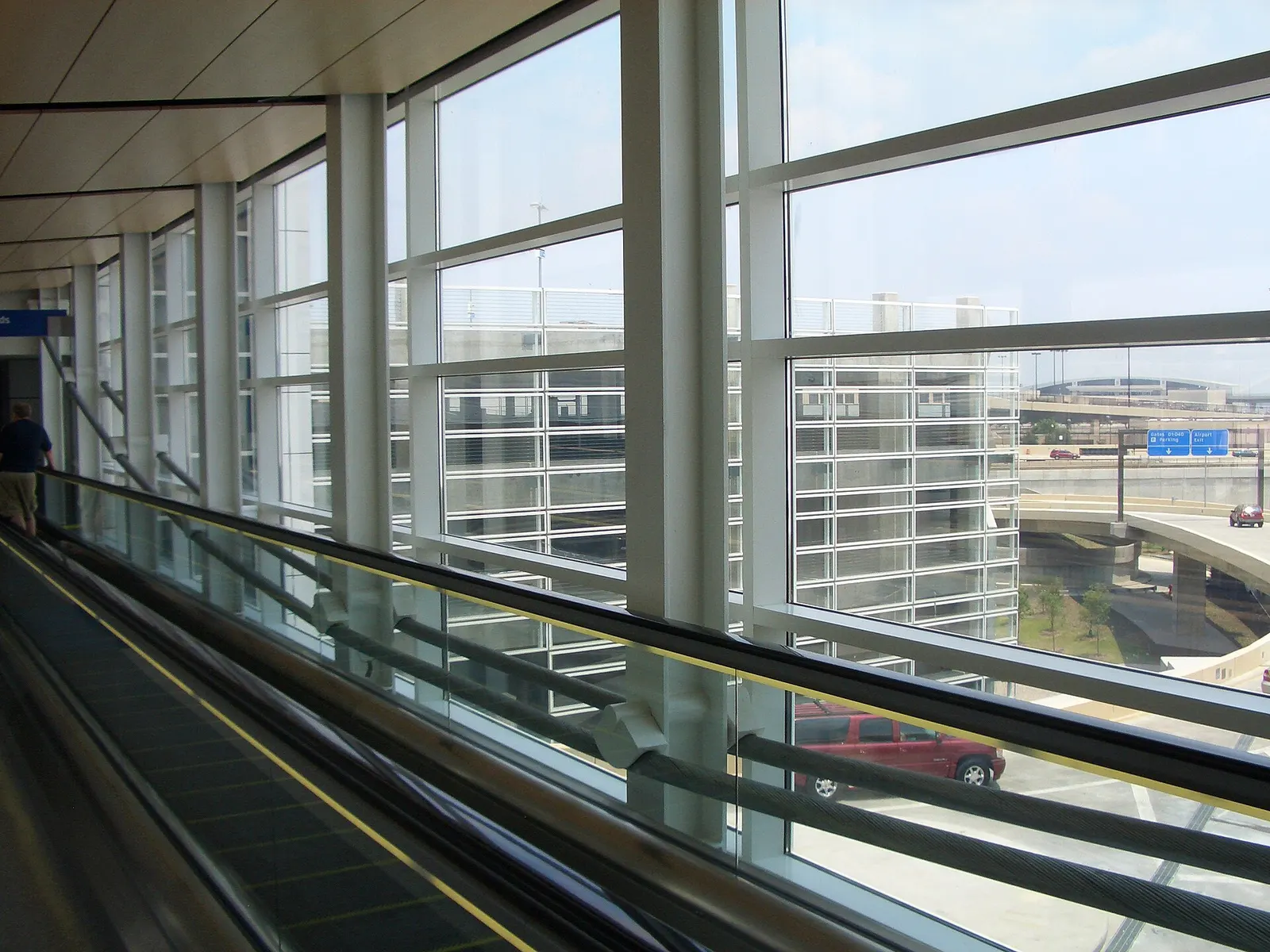 A cable-suspended glass footbridge inside DFW Terminal D spanning above the concourse below.
