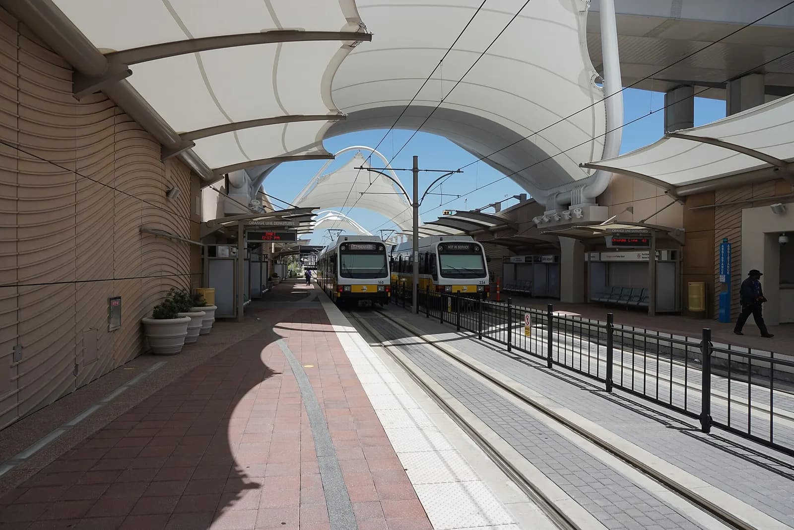 A DART Orange Line light-rail train stopped at the DFW Airport Station platform with airport structures visible beyond the tracks.