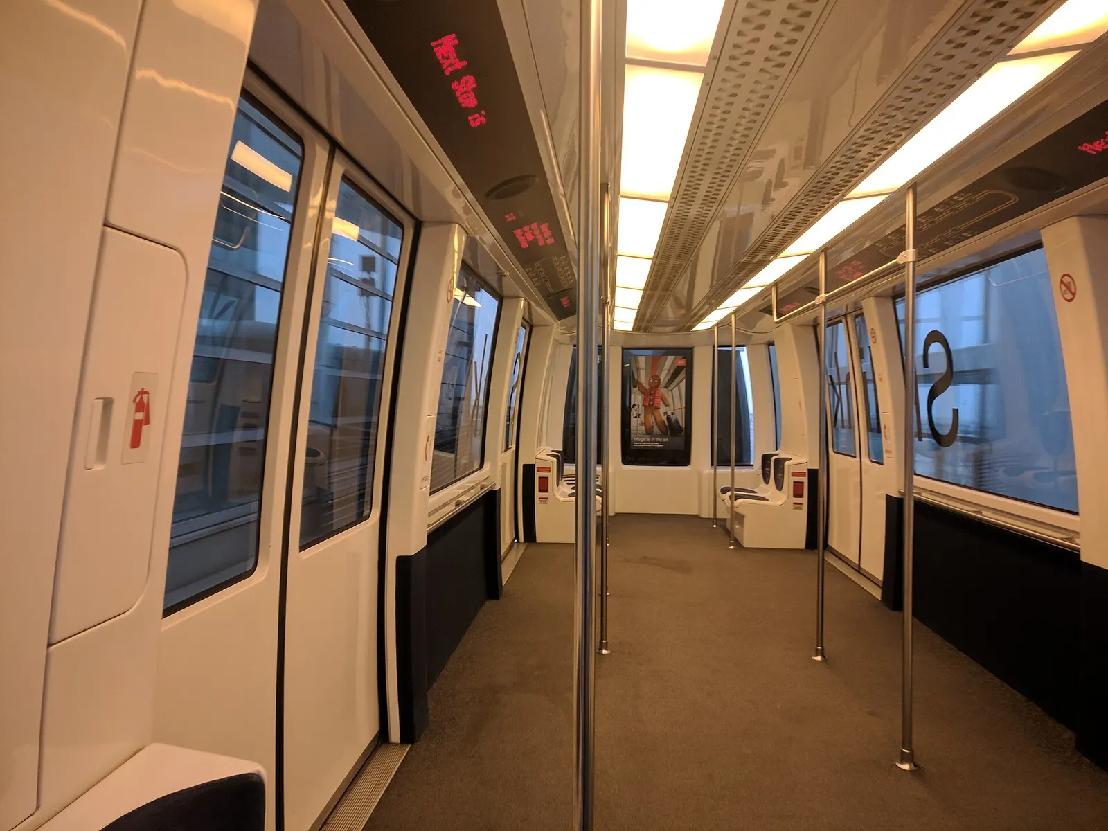 Inside a DFW Skylink automated people-mover car with empty blue seats as the train passes through a glass-walled corridor beside Terminal D.