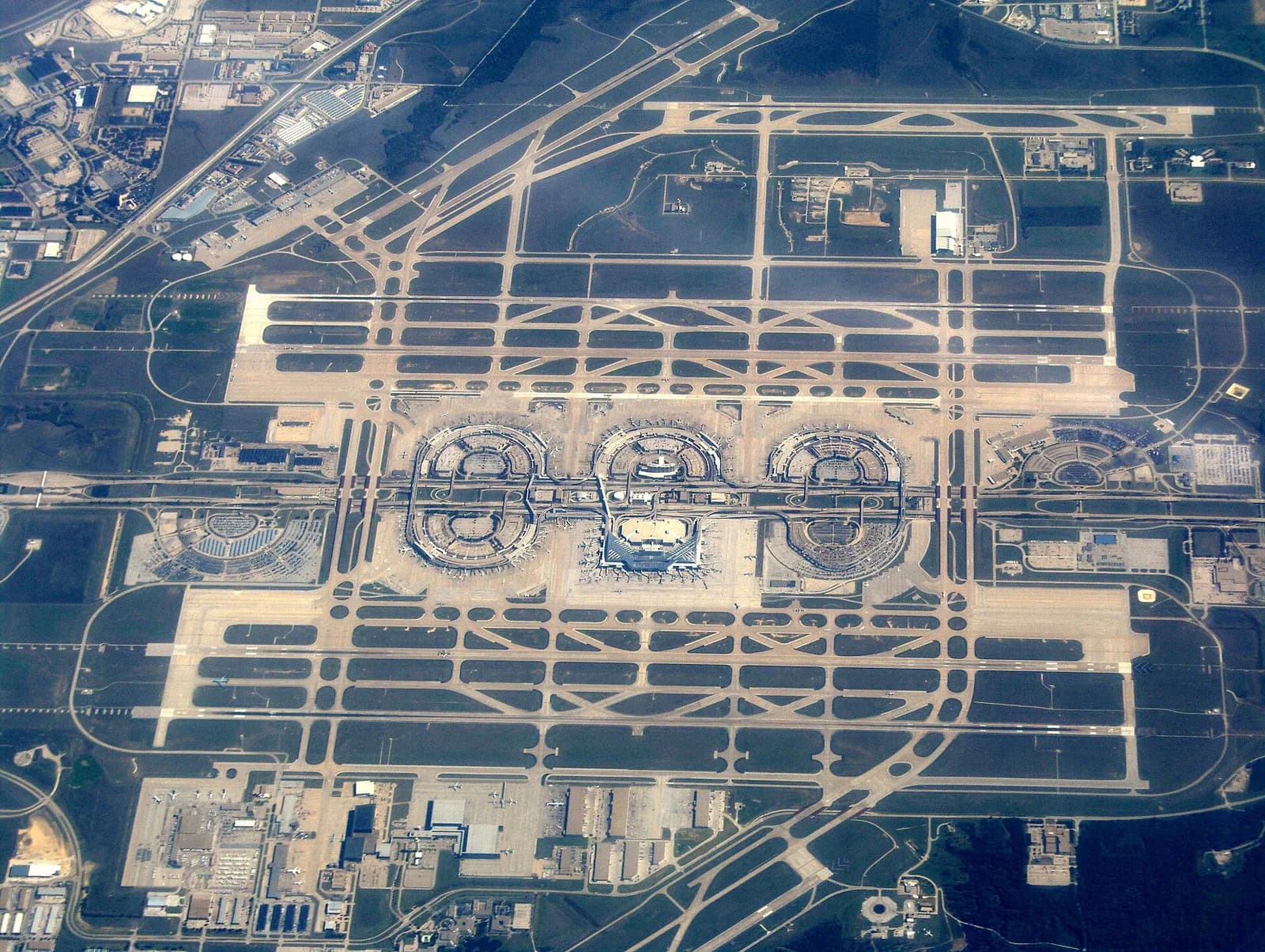 Aerial photograph of Dallas/Fort Worth International Airport showing the semi-circular terminal buildings, parking areas, and runways spread across a flat Texas landscape.