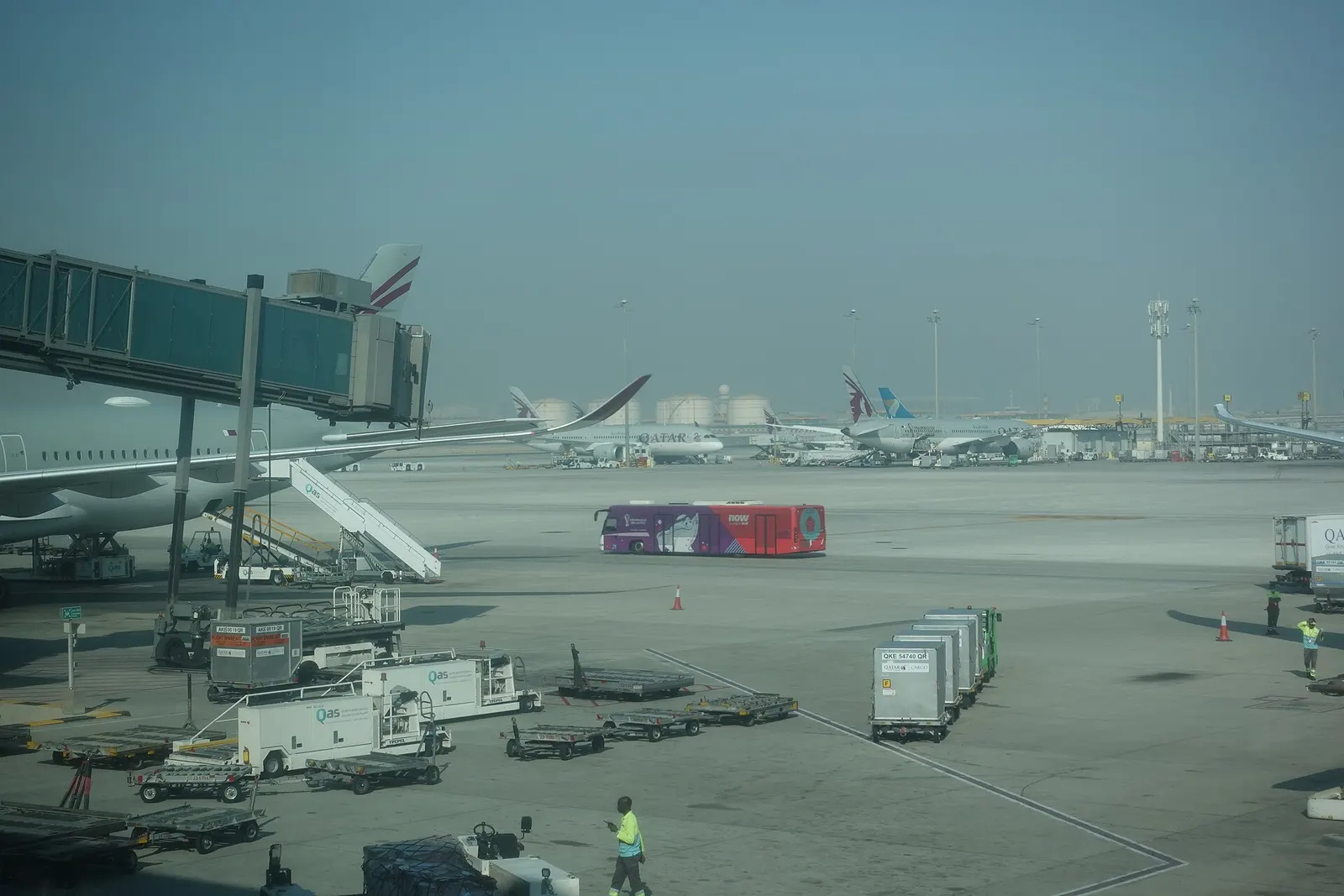 A Qatar Airways passenger transfer bus driving along the apron in front of Terminal A at Hamad International Airport.