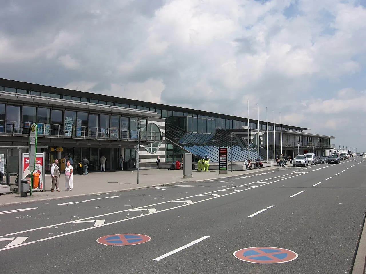 Landside curb of Dortmund Airport terminal with winged rhinoceros sculpture and bus stop