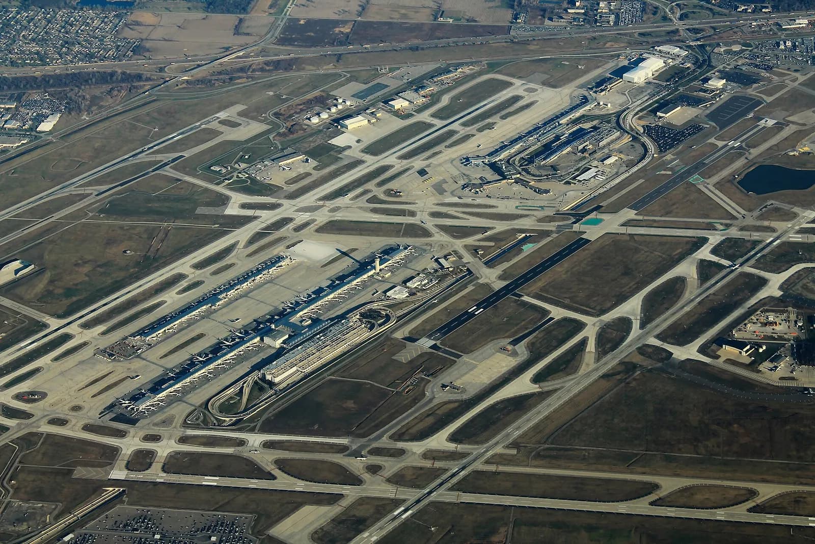An aerial view of Detroit Metropolitan Airport showing the McNamara and North terminals, parallel runways, and surrounding Romulus countryside.