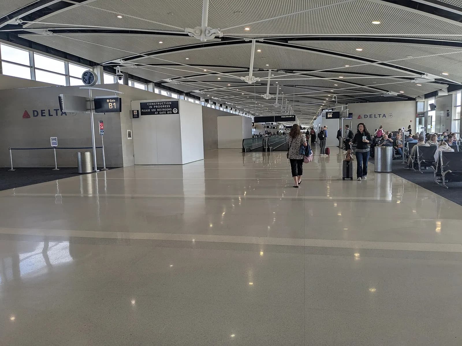 A spacious Concourse B gate area with seating, flight information displays, and floor-to-ceiling windows overlooking the ramp at Detroit Metropolitan Airport.