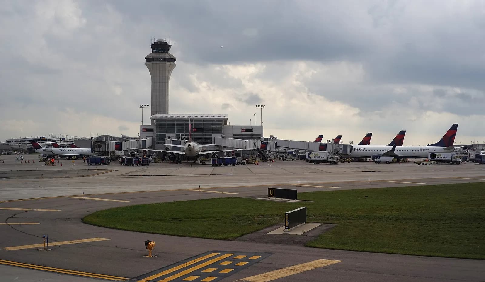 Wide exterior view of the curved glass-and-steel McNamara Terminal at Detroit Metropolitan Wayne County Airport under a partly cloudy sky.