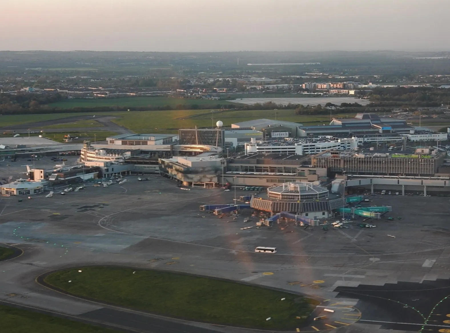 A panoramic landside view across Dublin Airport showing terminal roofs, control tower, and aircraft parked at gates.