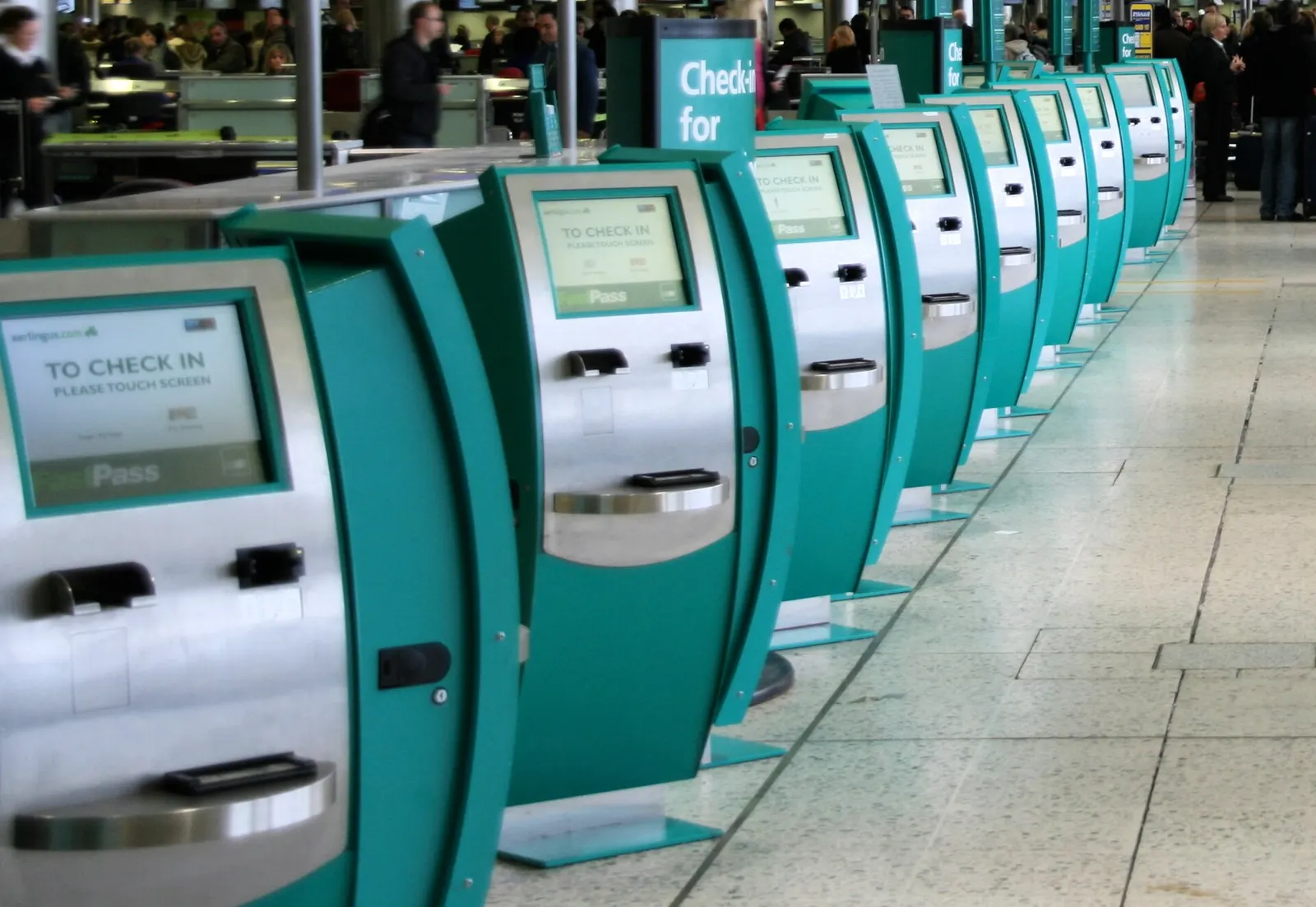 A row of Aer Lingus self-service check-in kiosks with touchscreen displays in the departures hall at Dublin Airport.