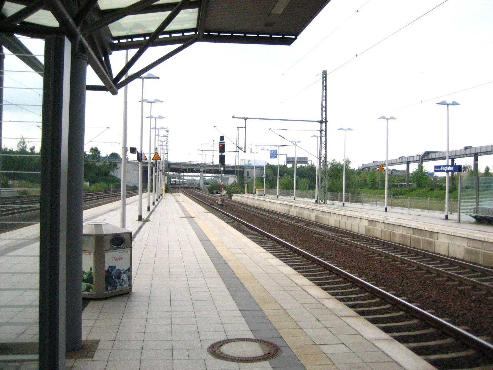 Covered platforms and wayfinding signs at Düsseldorf Flughafen S-Bahn station below the airport terminals.