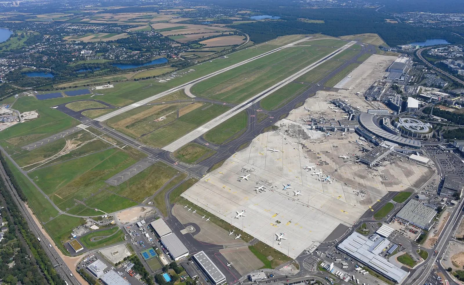 Aerial view of Düsseldorf Airport showing parallel runways, the terminal complex, taxiways, and surrounding roads and parking.