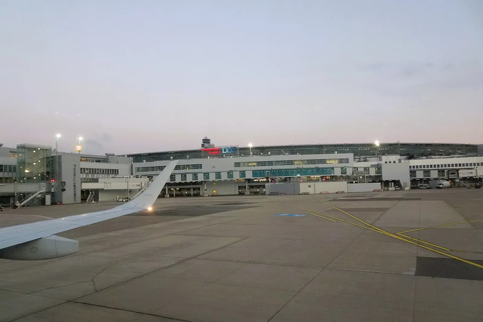 The glass-fronted main terminal of Düsseldorf Airport with its curved roofline and DUS signage, photographed from the approach area on a clear day.