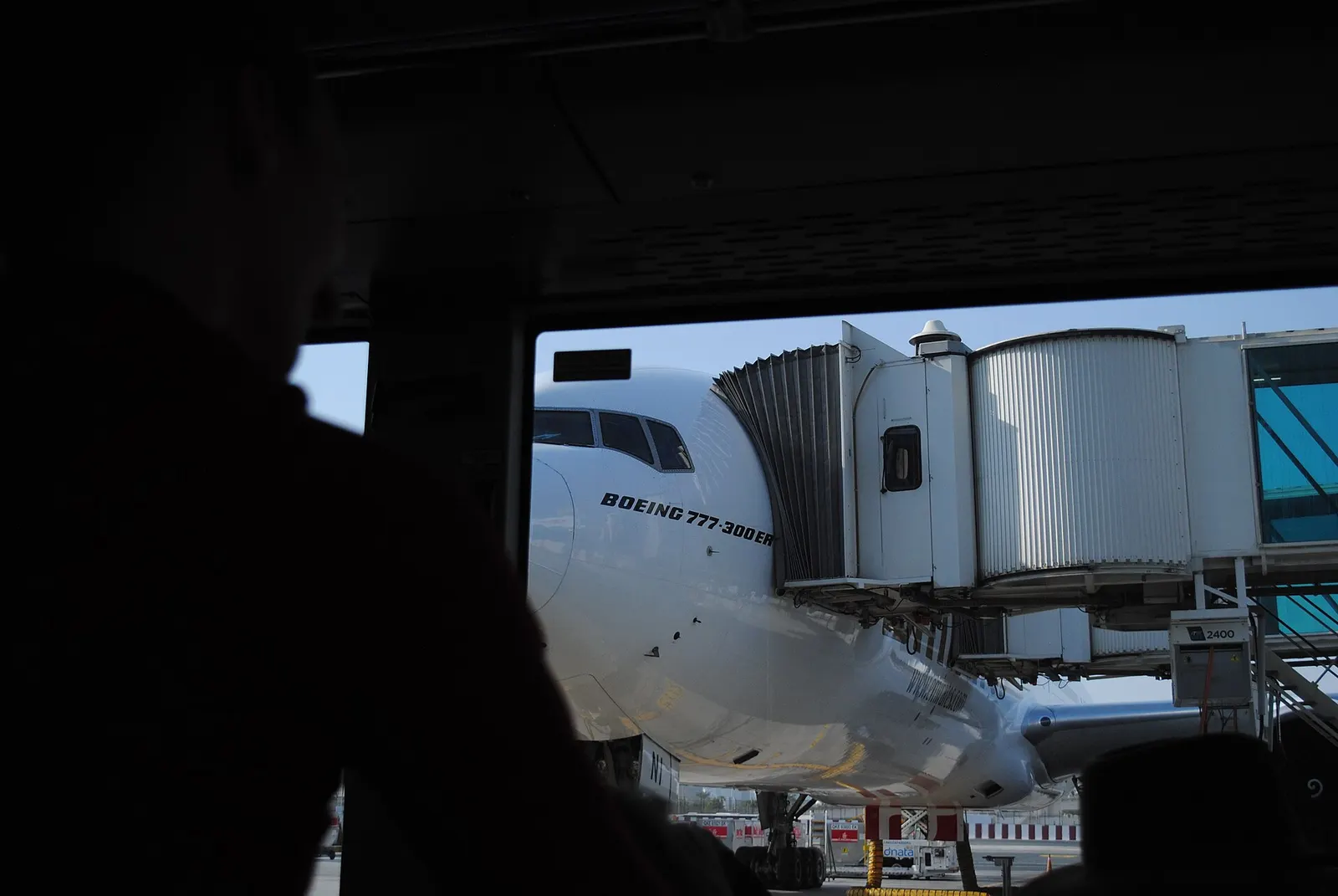 A pre-dawn view through a shuttle-bus window toward Terminal 2 jet bridges and parked aircraft on the ramp.