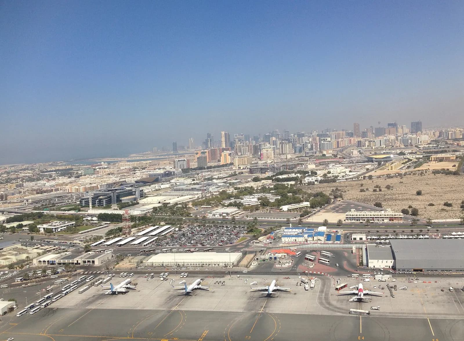 A ground-level view of Dubai International Airport terminal buildings and airfield infrastructure under a clear sky.