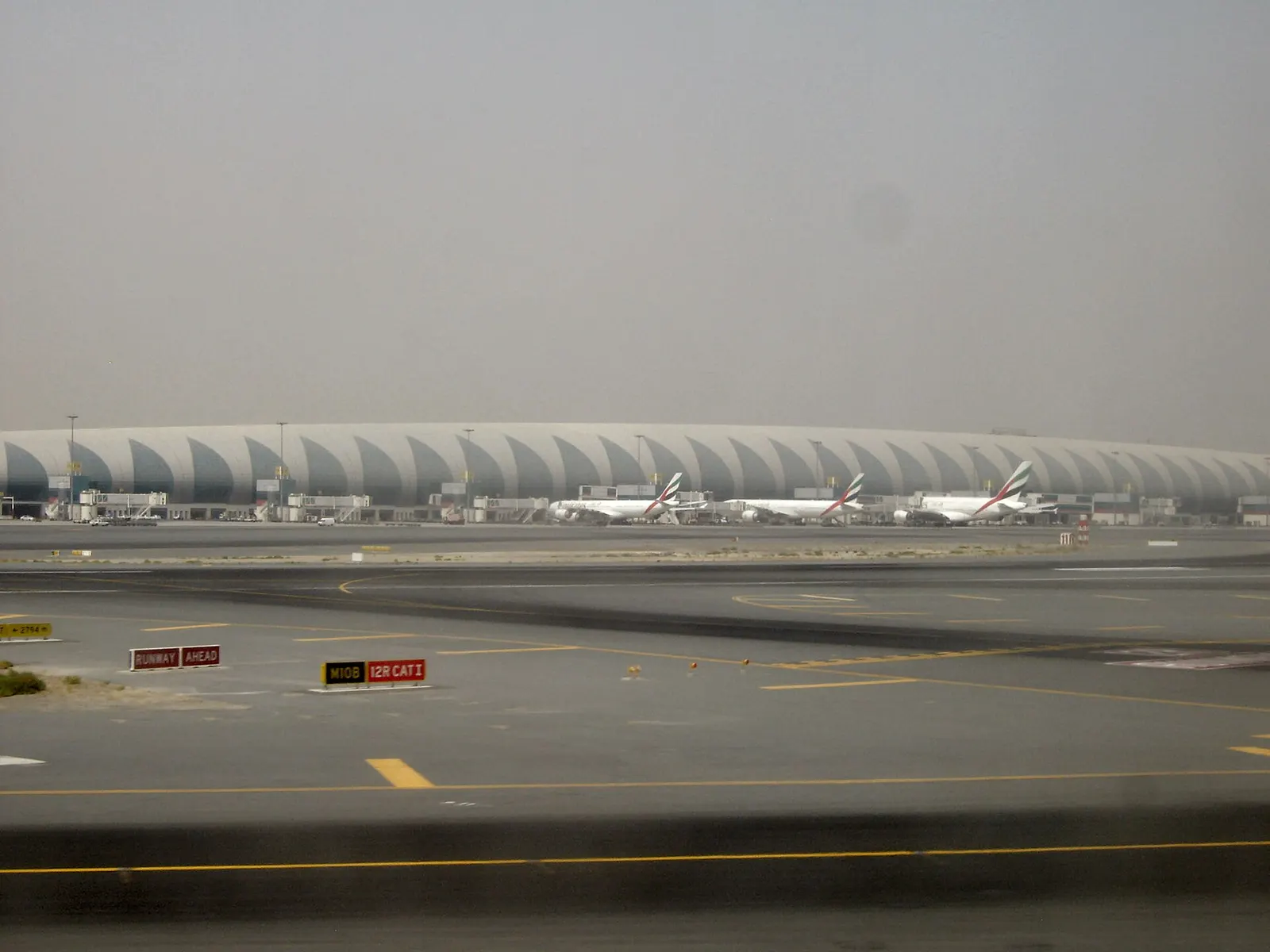 Inside Terminal 3 concourse with high ceilings, gate areas, and aircraft visible on the ramp beyond.