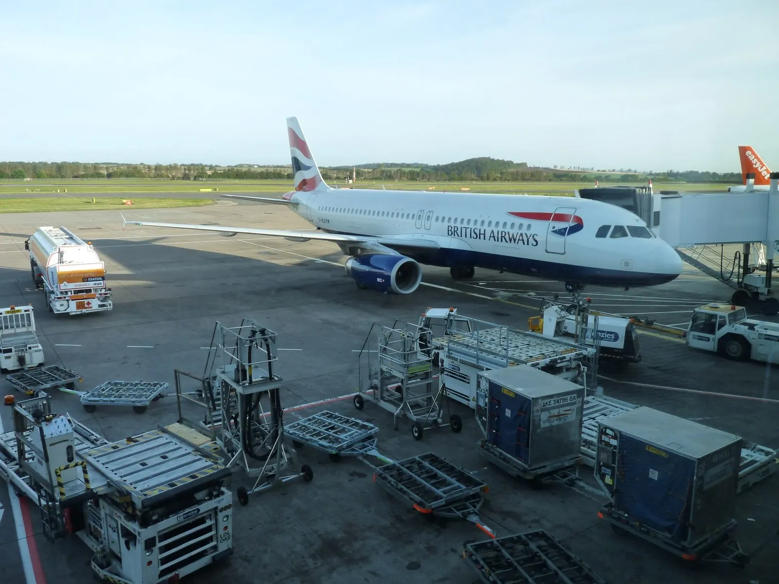 A British Airways aircraft parked at a jet bridge gate on the Edinburgh Airport apron with the terminal building behind it.