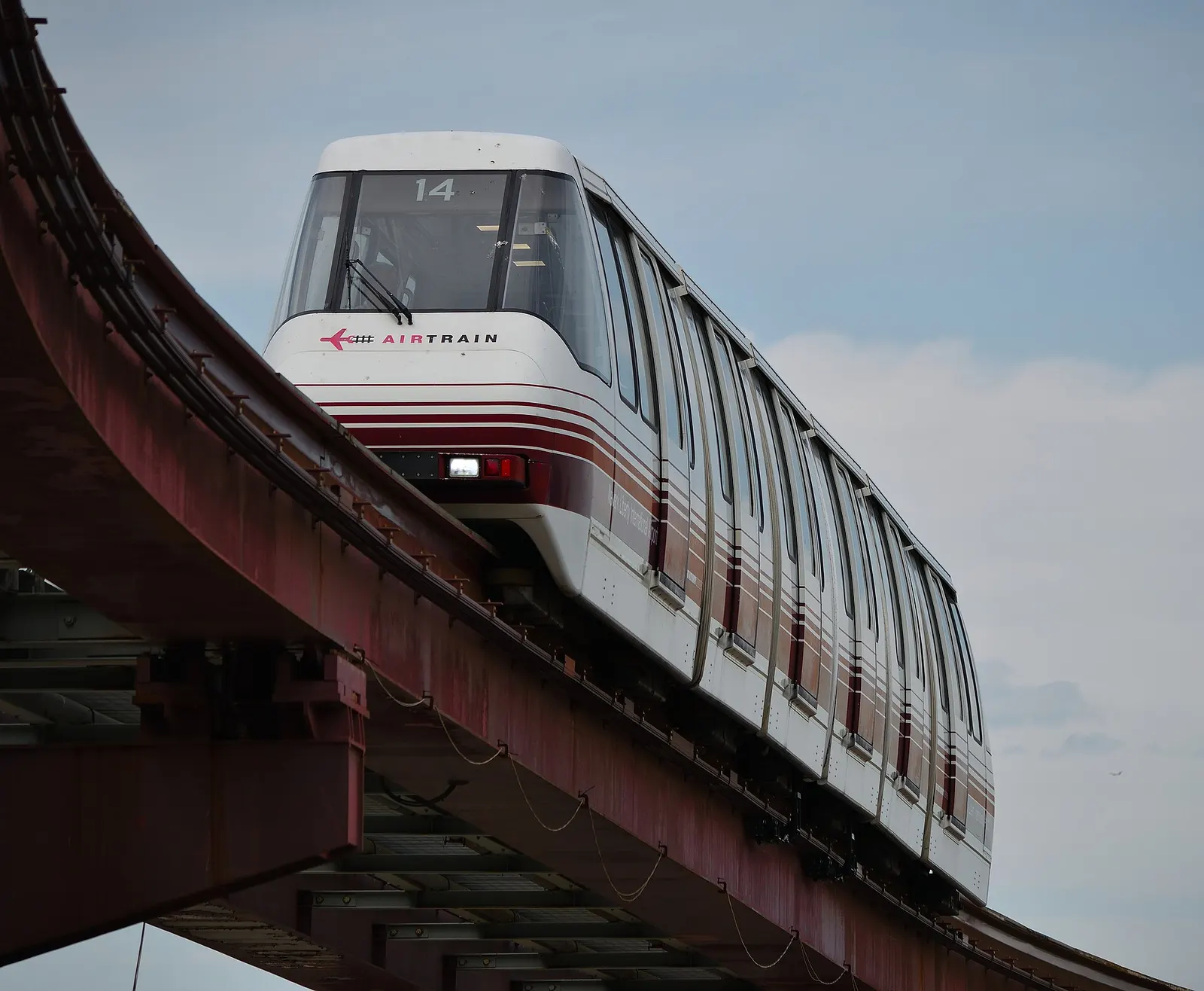 A silver AirTrain monorail car approaches the elevated Terminal A station on an outdoor guideway.