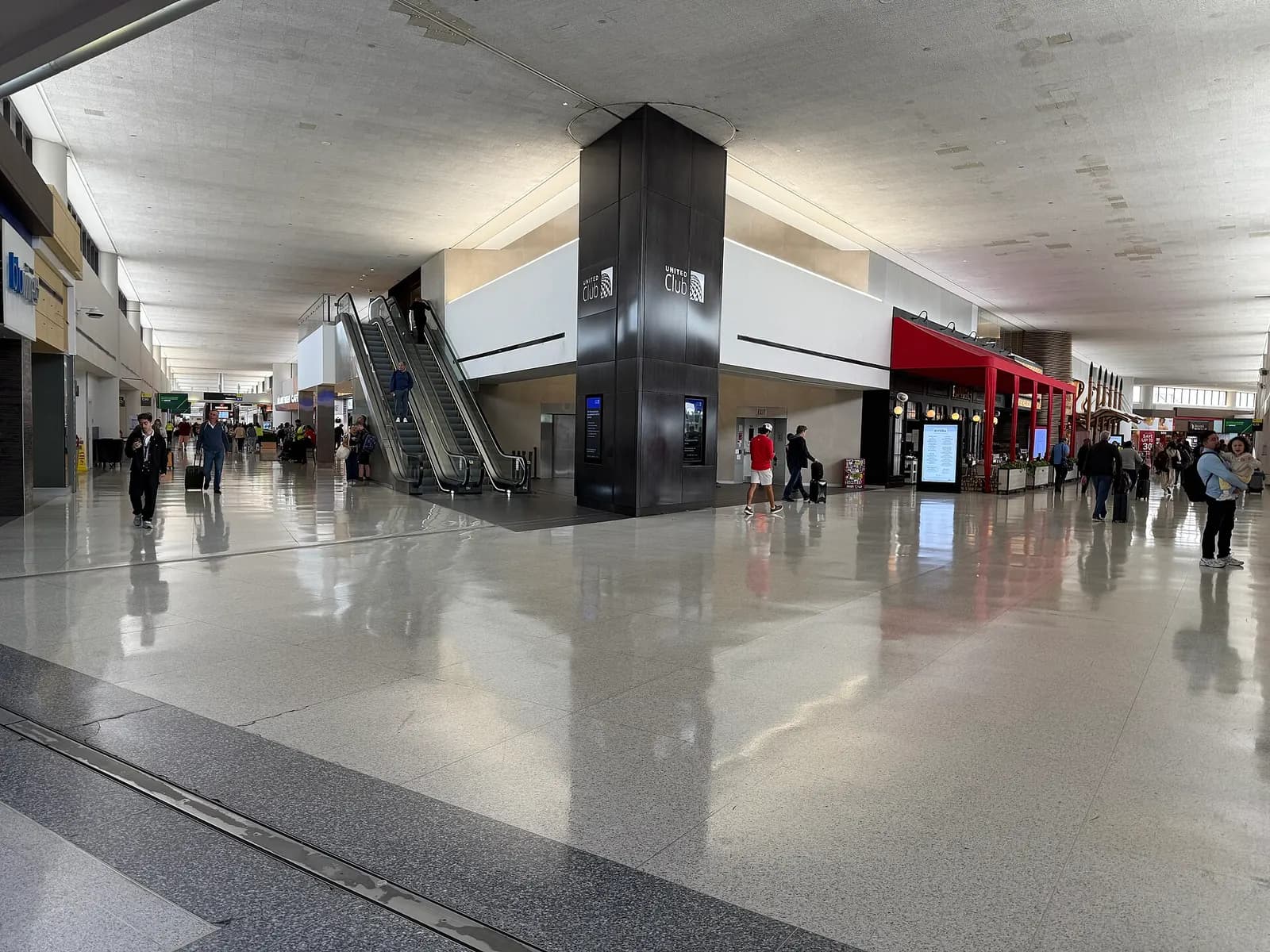 A wide concourse inside Terminal C with moving walkways, gate signage, and United Airlines branding.