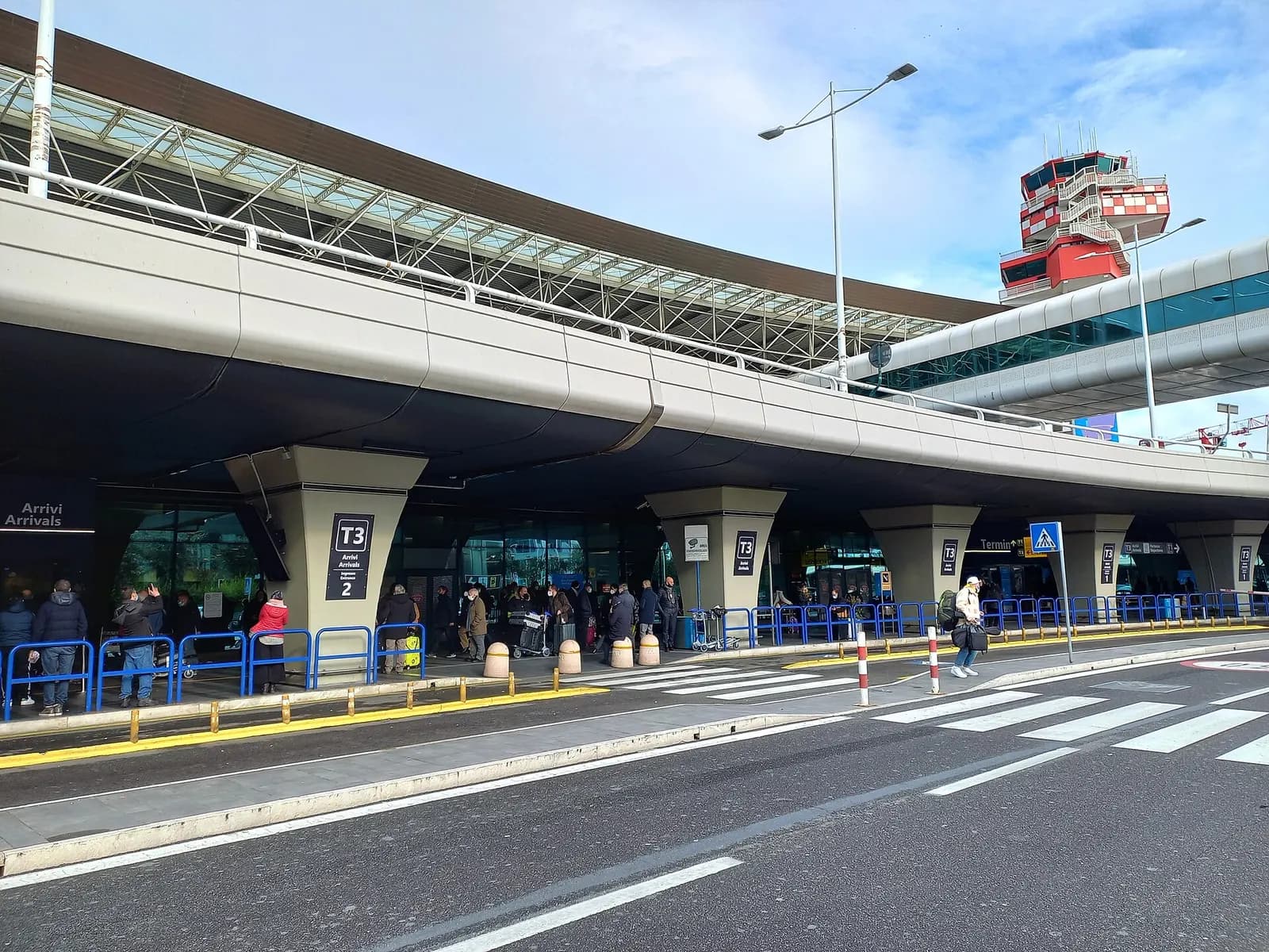 Ground-level view of Aeroporto di Roma-Fiumicino showing terminal exteriors, roadways, and airport signage.