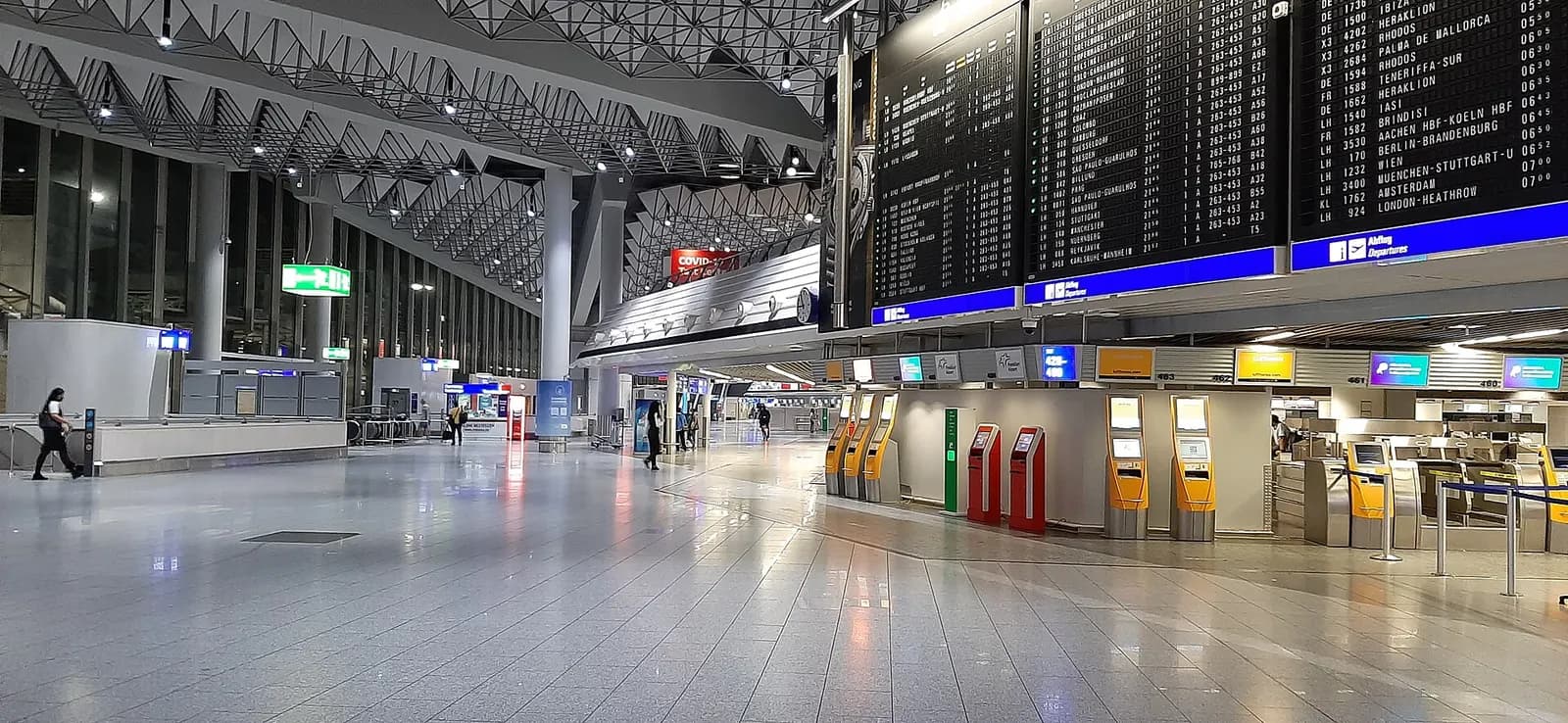 Wide view of the Terminal 1 departure entrance hall at Frankfurt Airport with a high glass facade, departure signage, and travelers moving through the main doors.