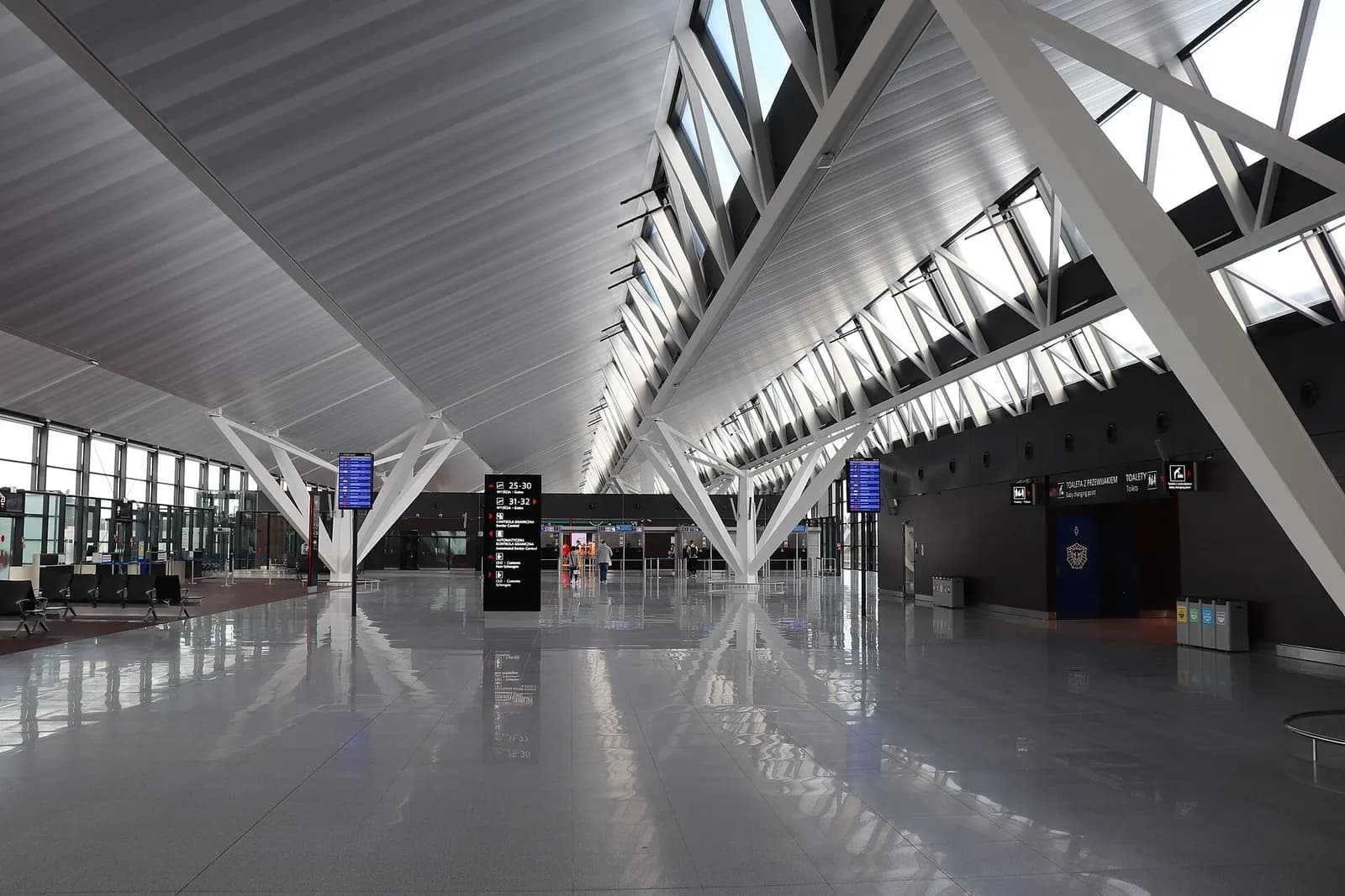 Spacious, brightly lit departure hall inside Terminal 2 with high ceilings, signage, and passengers moving through the concourse.