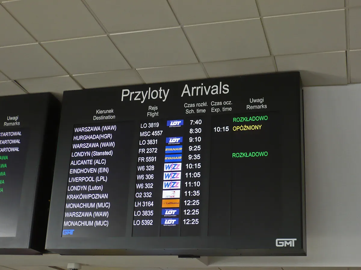 Electronic arrivals flight information display board listing incoming flights on a screen in the Gdańsk airport terminal.
