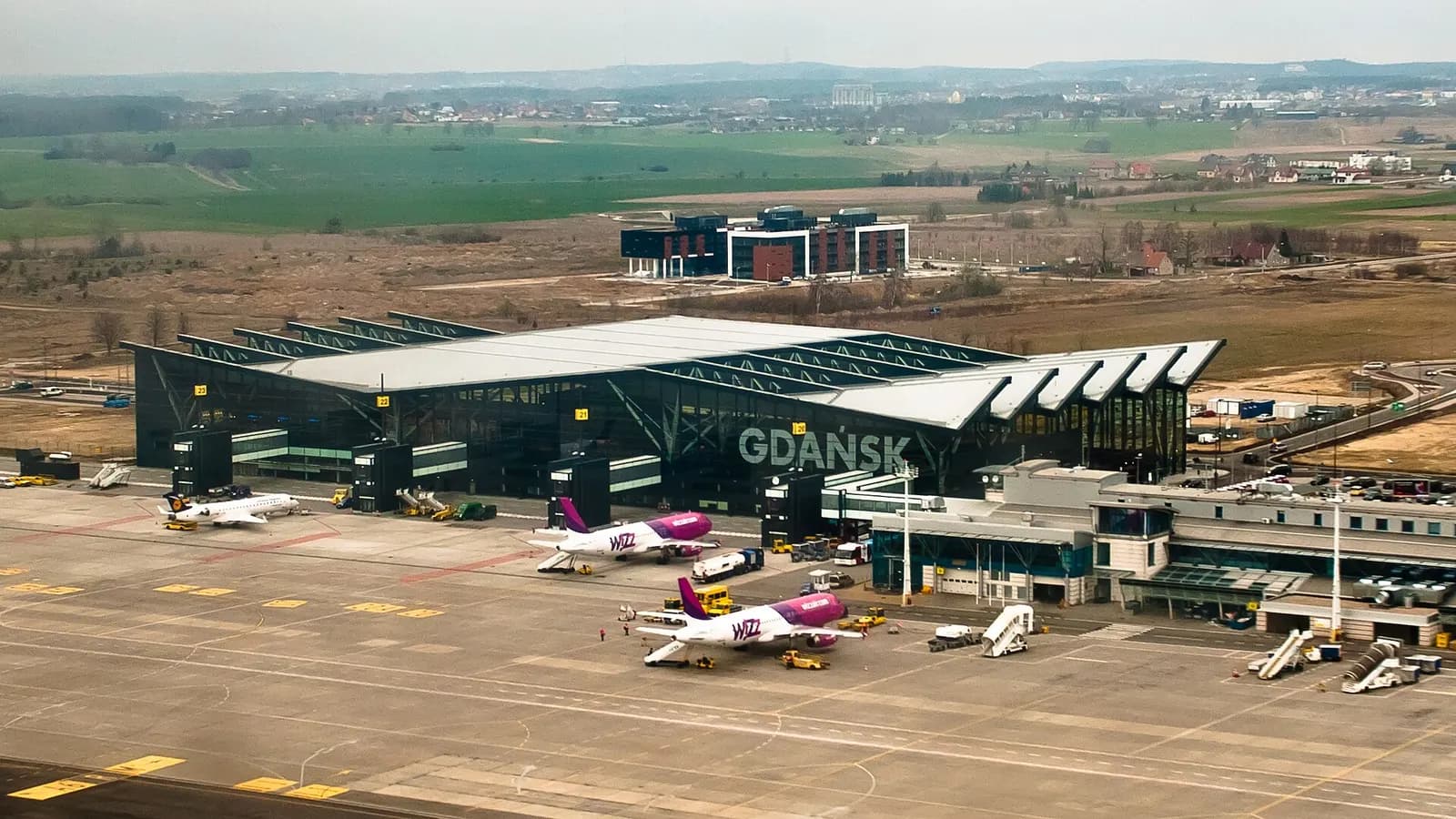 Wide exterior of the modern Terminal 2 at Gdańsk Lech Wałęsa Airport, with glass facades and a paved forecourt in front.