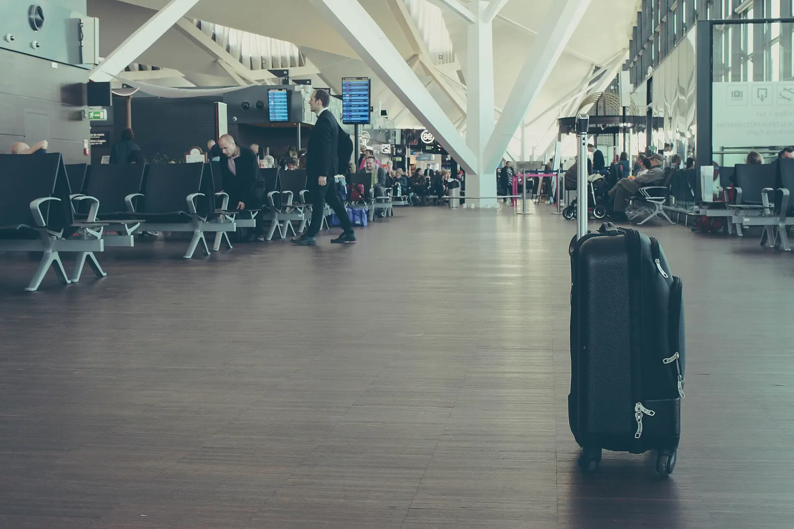 Travelers standing and walking in the contemporary passenger terminal interior at Gdańsk Lech Wałęsa Airport.