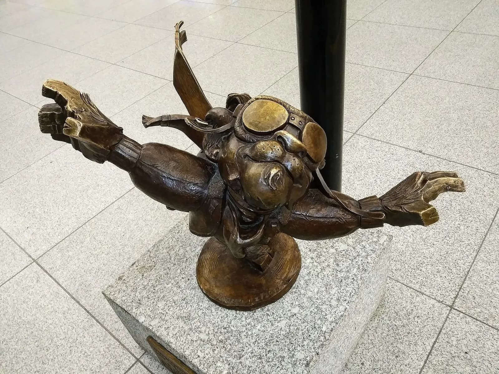 Bronze statue of Hewelion the Aviator, a cartoon lion figure in aviator gear, displayed inside Gdańsk airport.