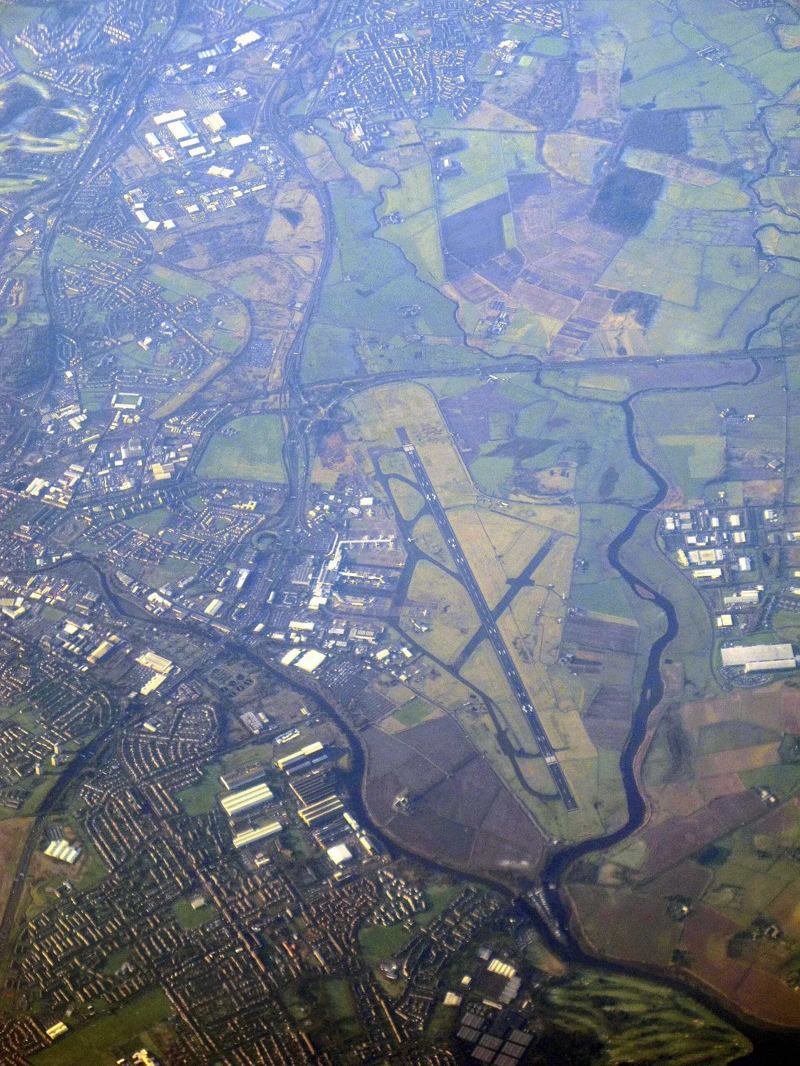 Aerial view of Glasgow Airport with its runways, terminal buildings, and surrounding green countryside and roads.